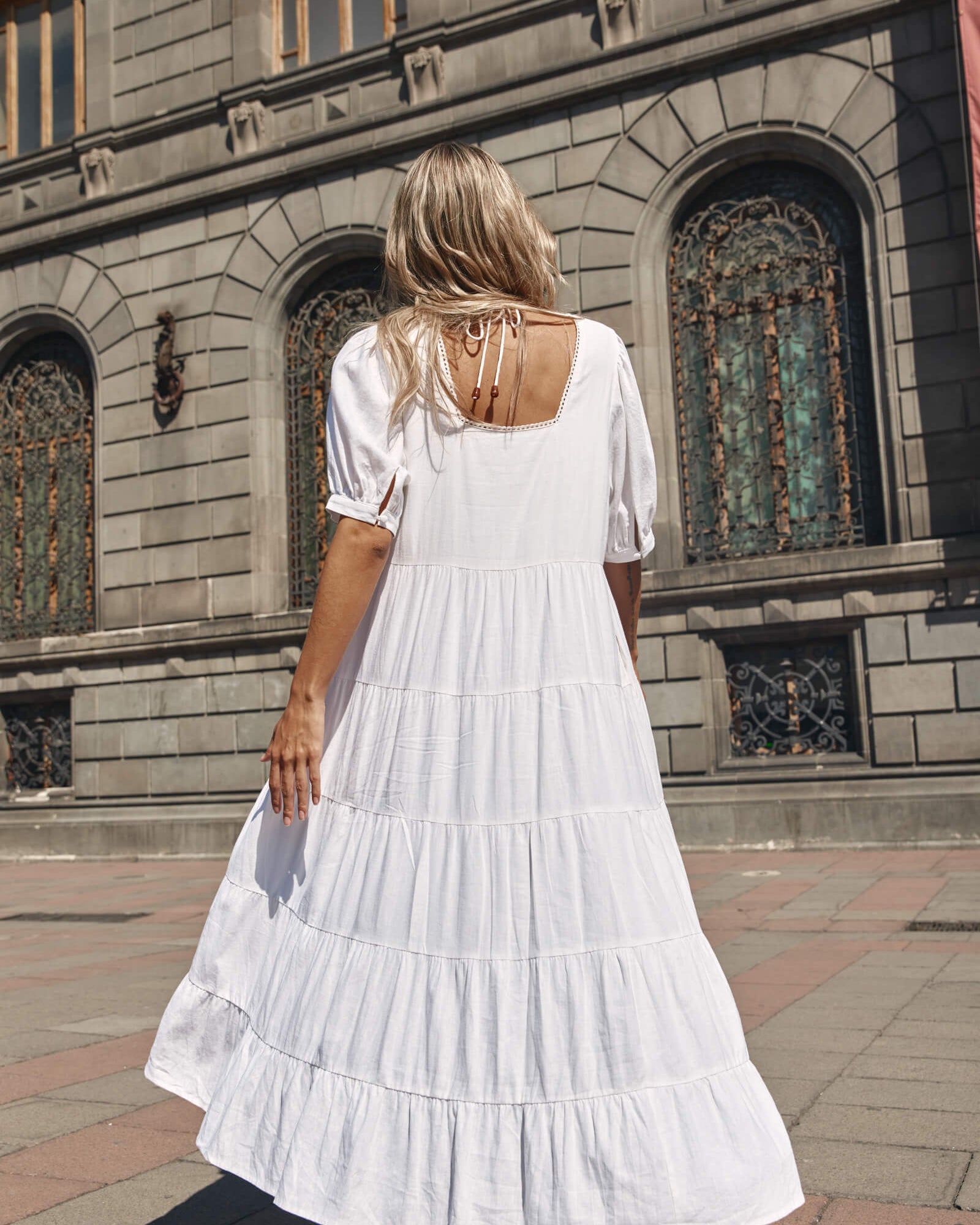 Back of a lady in a white tired dress in front of a grey building