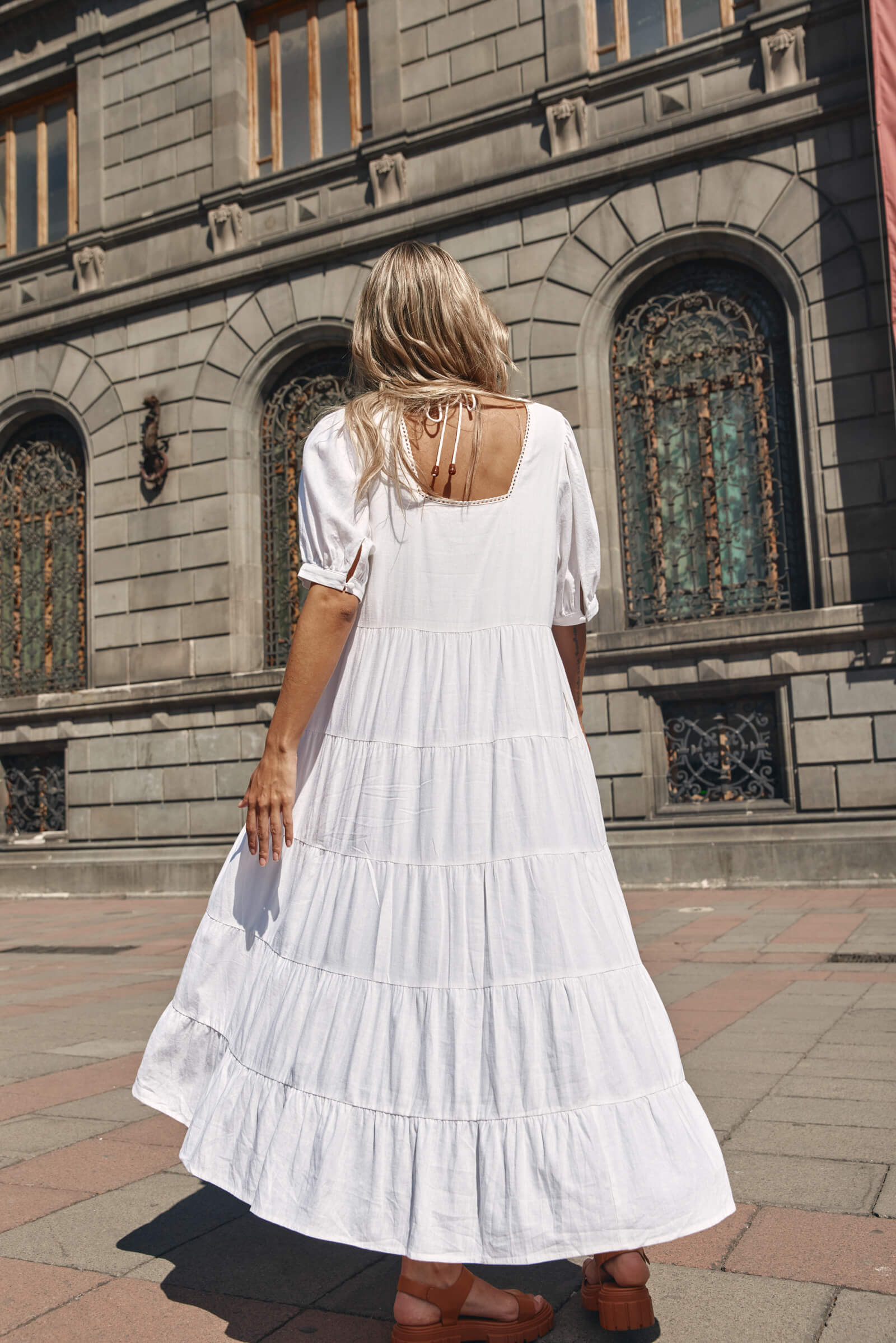 Back of a lady in a white tired dress in front of a grey building