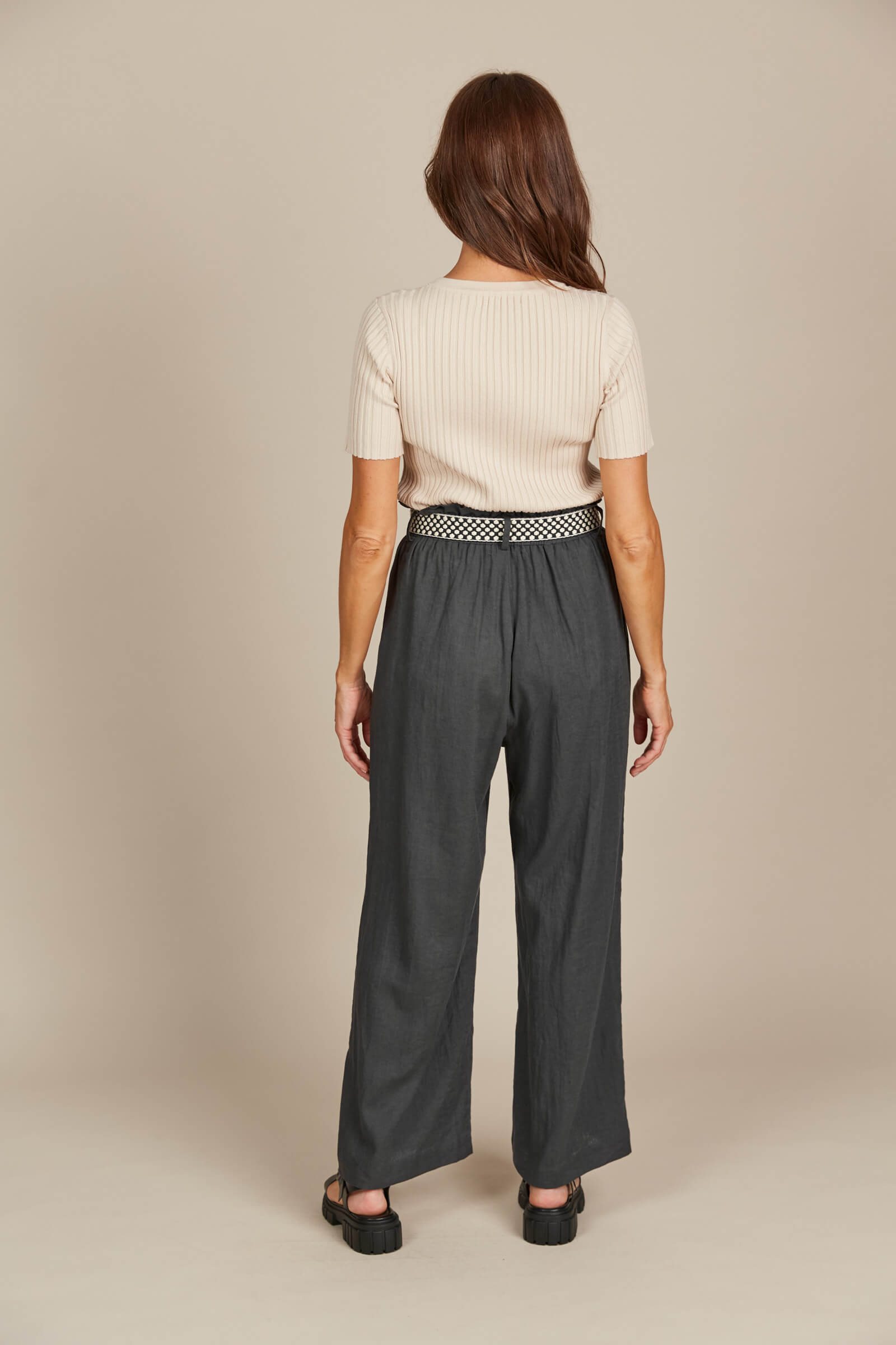 Model in grey pants with belt and cream top against a cream background