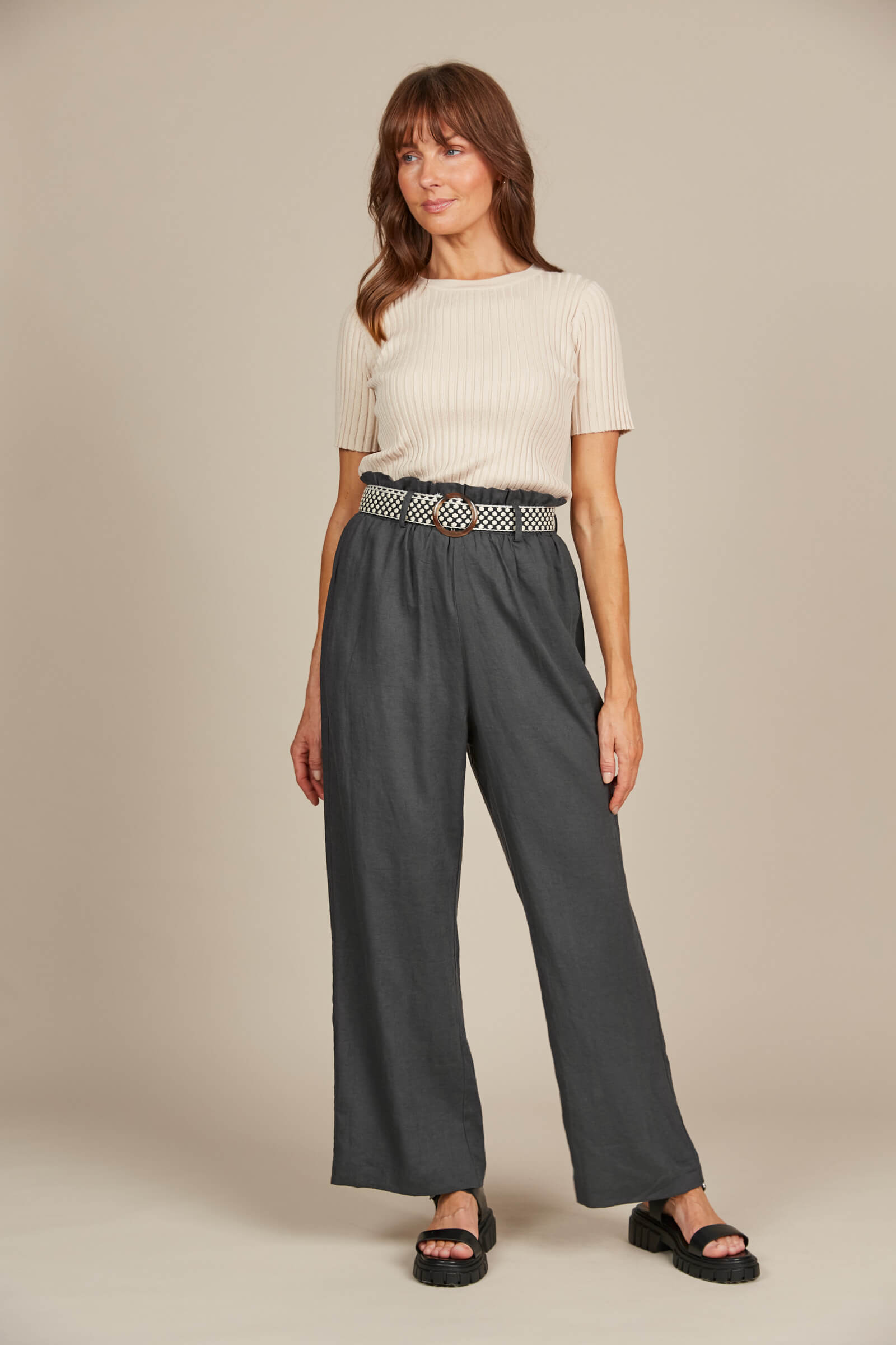 Model in grey pants with belt and cream top against a cream background