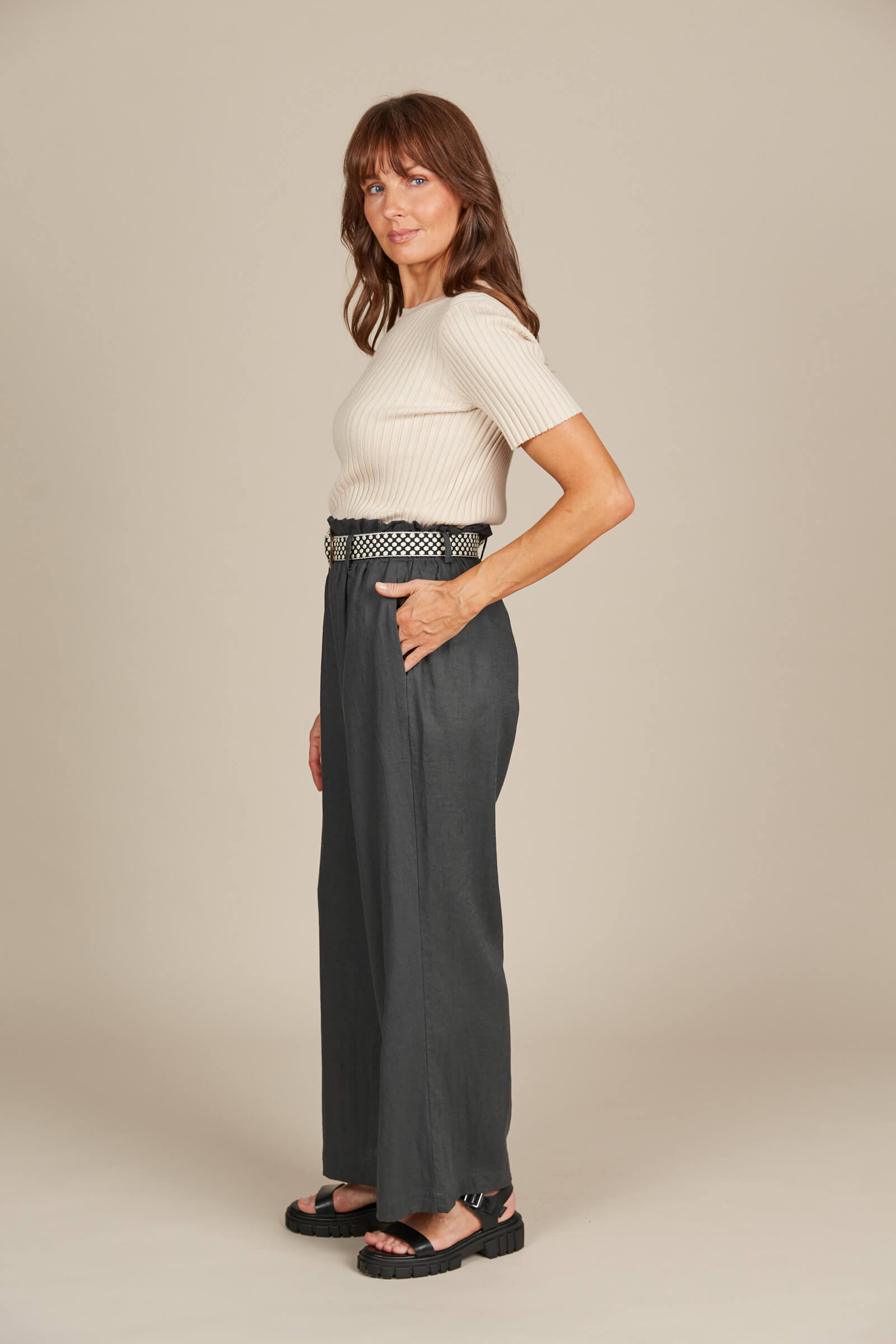 Model in grey pants with belt and cream top against a cream background