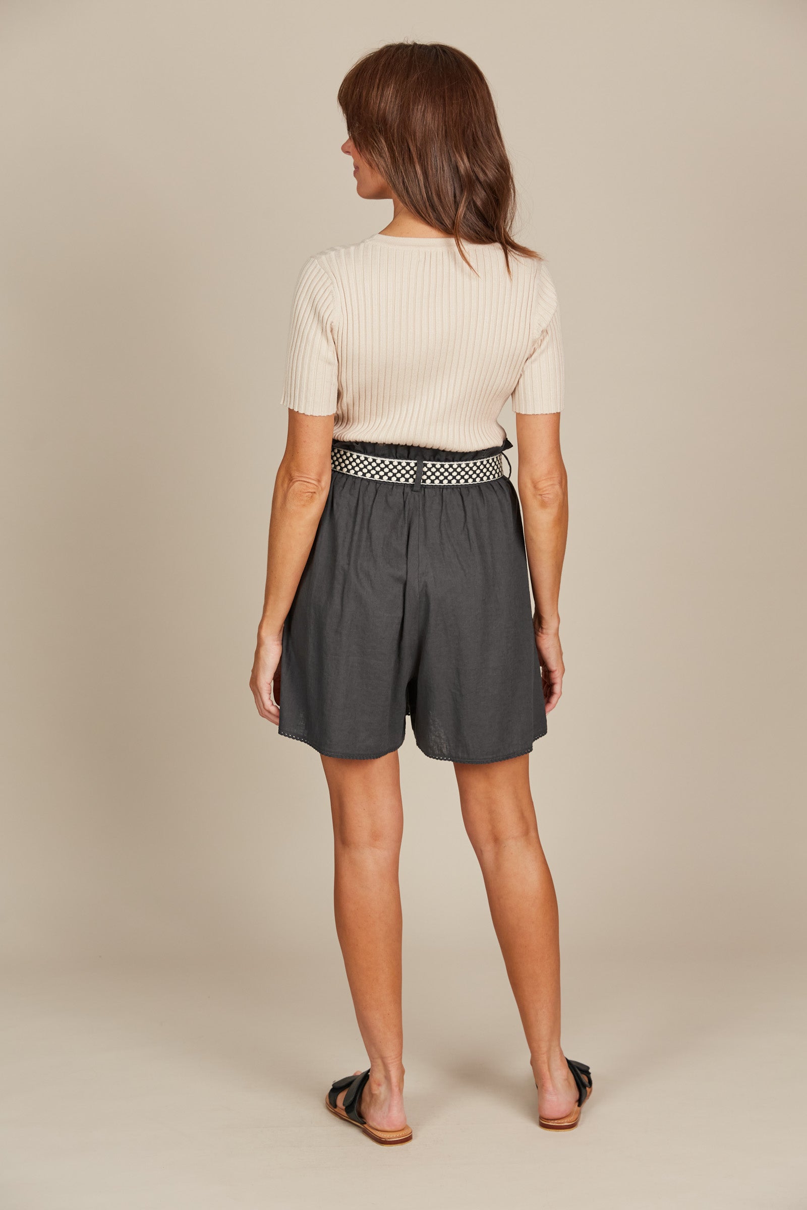 Woman in a fashionable outfit featuring a cream ribbed top and charcol grey shorts with black and white belt