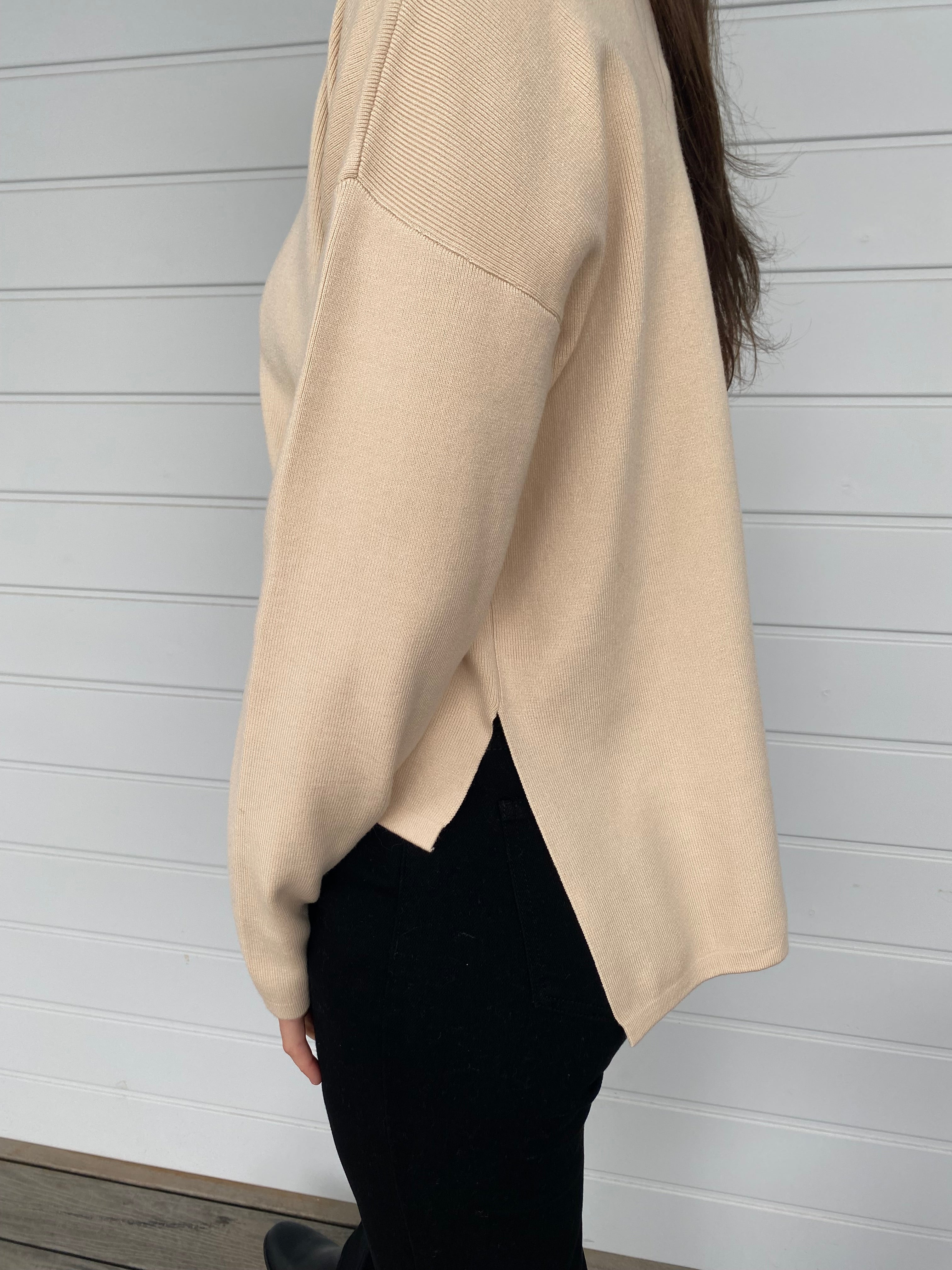 Women standing in a cream top and black denim jeans against a wall