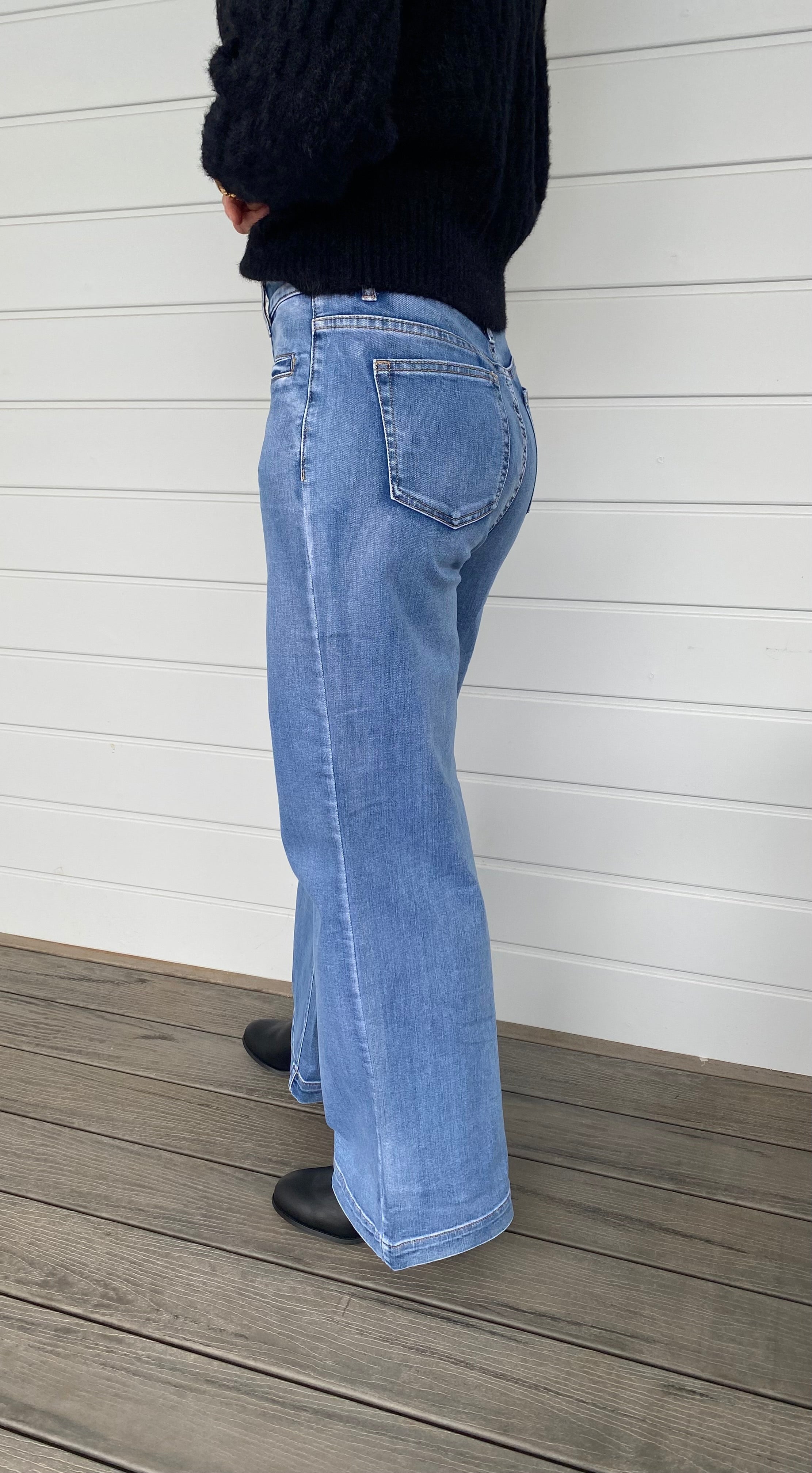 A stylish woman wearing a black sweater knit paired with wide-leg blue jeans, embodying a chic and casual look.