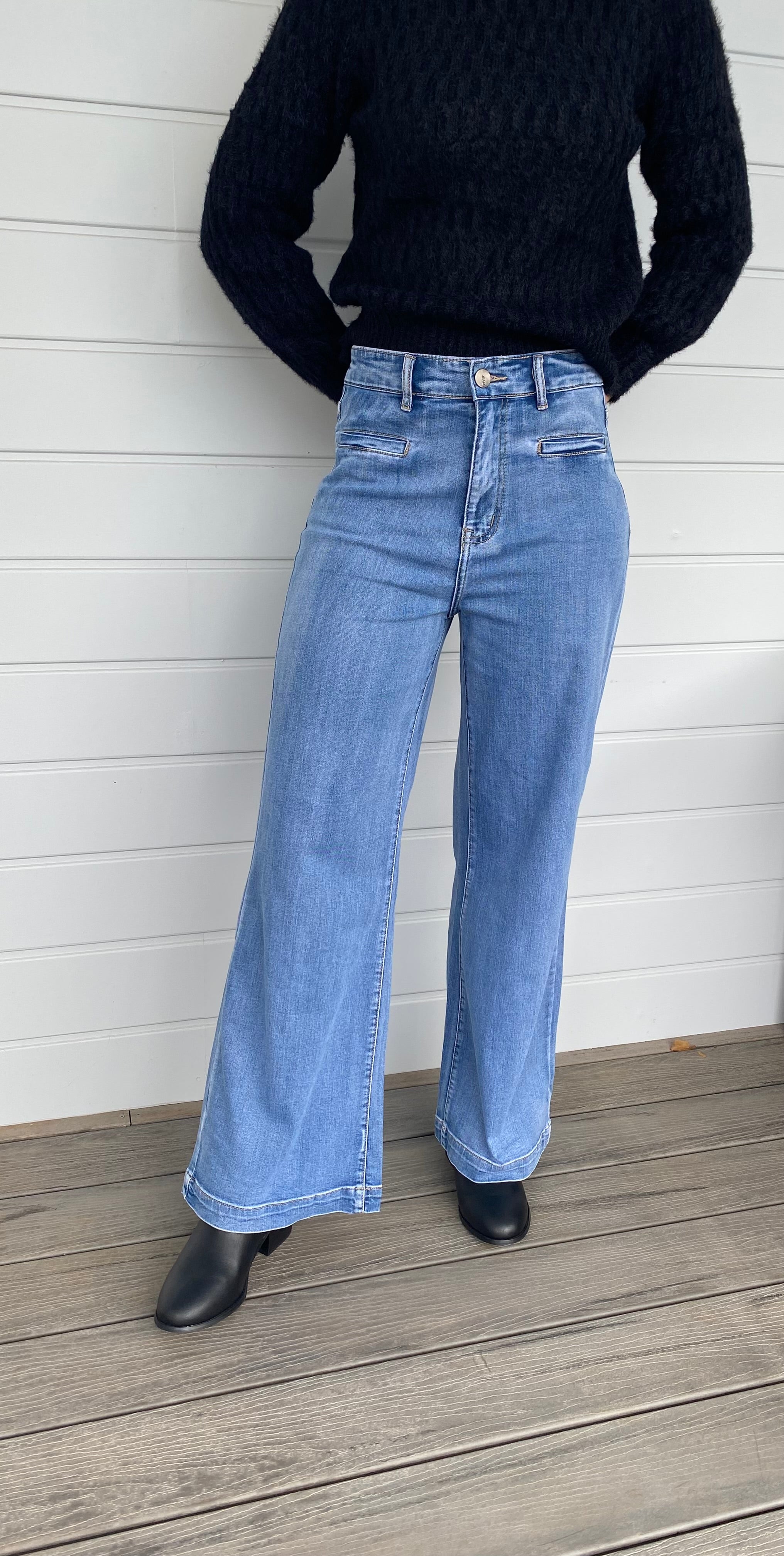 A stylish woman wearing a black sweater knit paired with wide-leg blue jeans, embodying a chic and casual look.