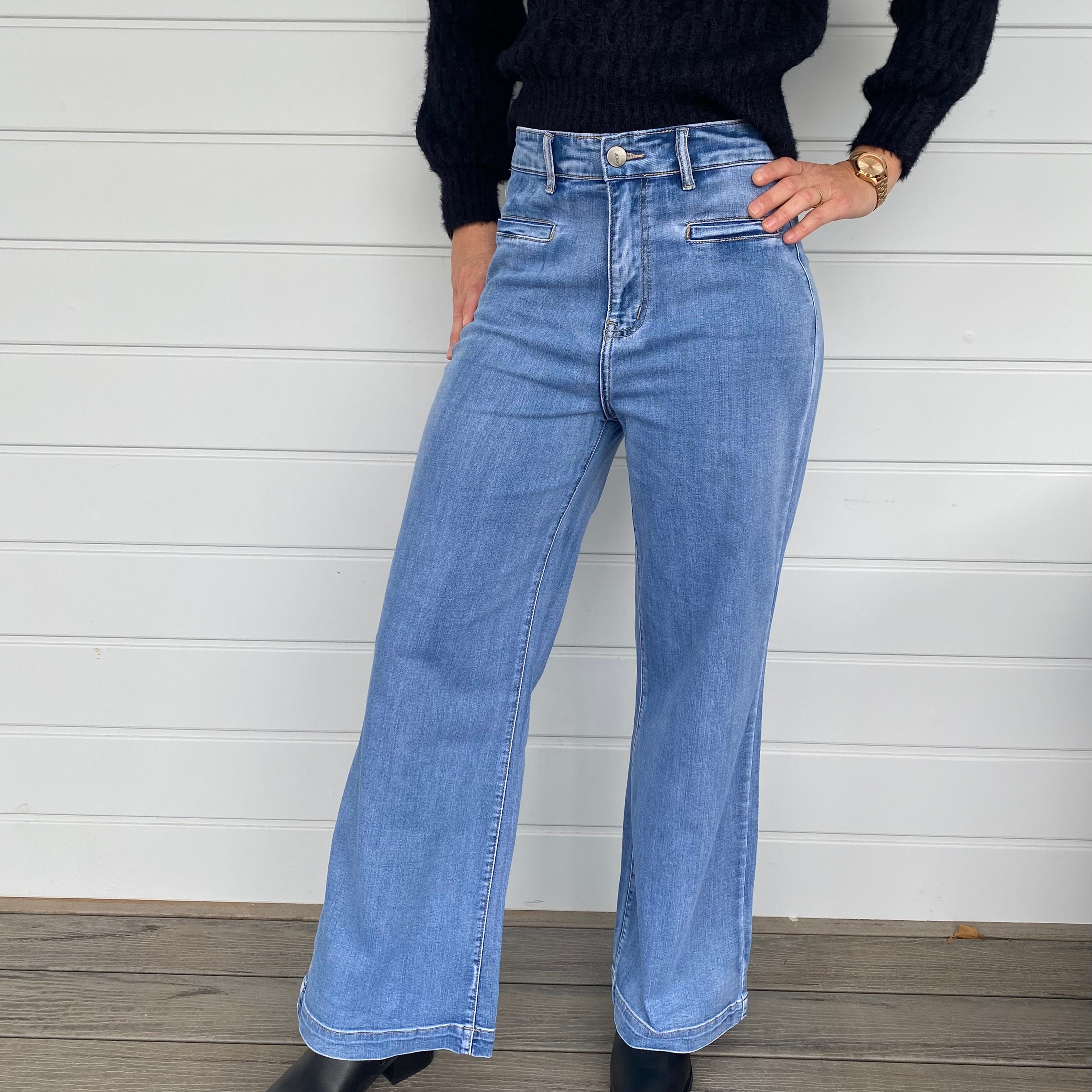 A stylish woman wearing a black sweater knit paired with wide-leg blue jeans, embodying a chic and casual look.