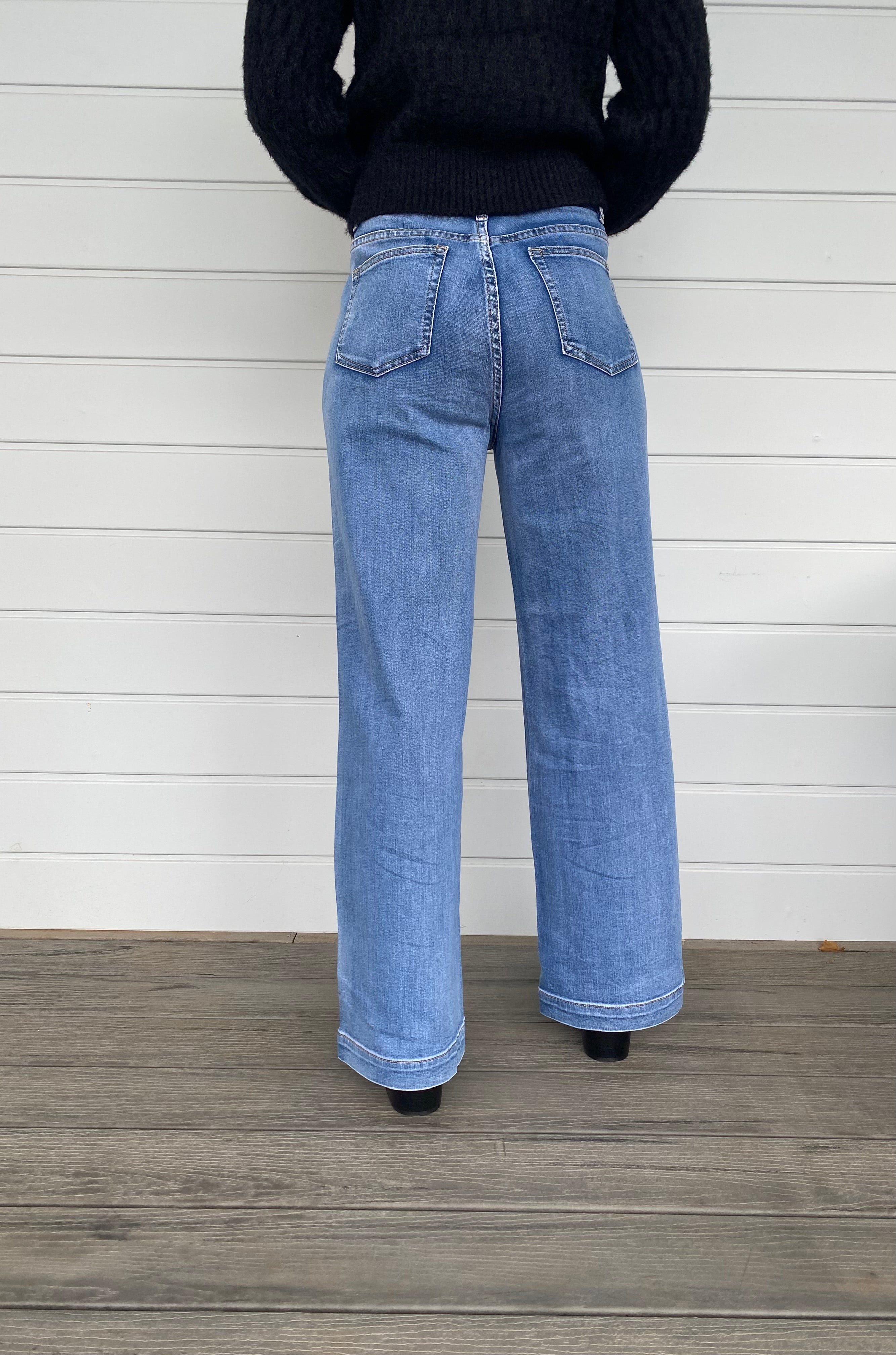 A stylish woman wearing a black sweater knit paired with wide-leg blue jeans, embodying a chic and casual look.