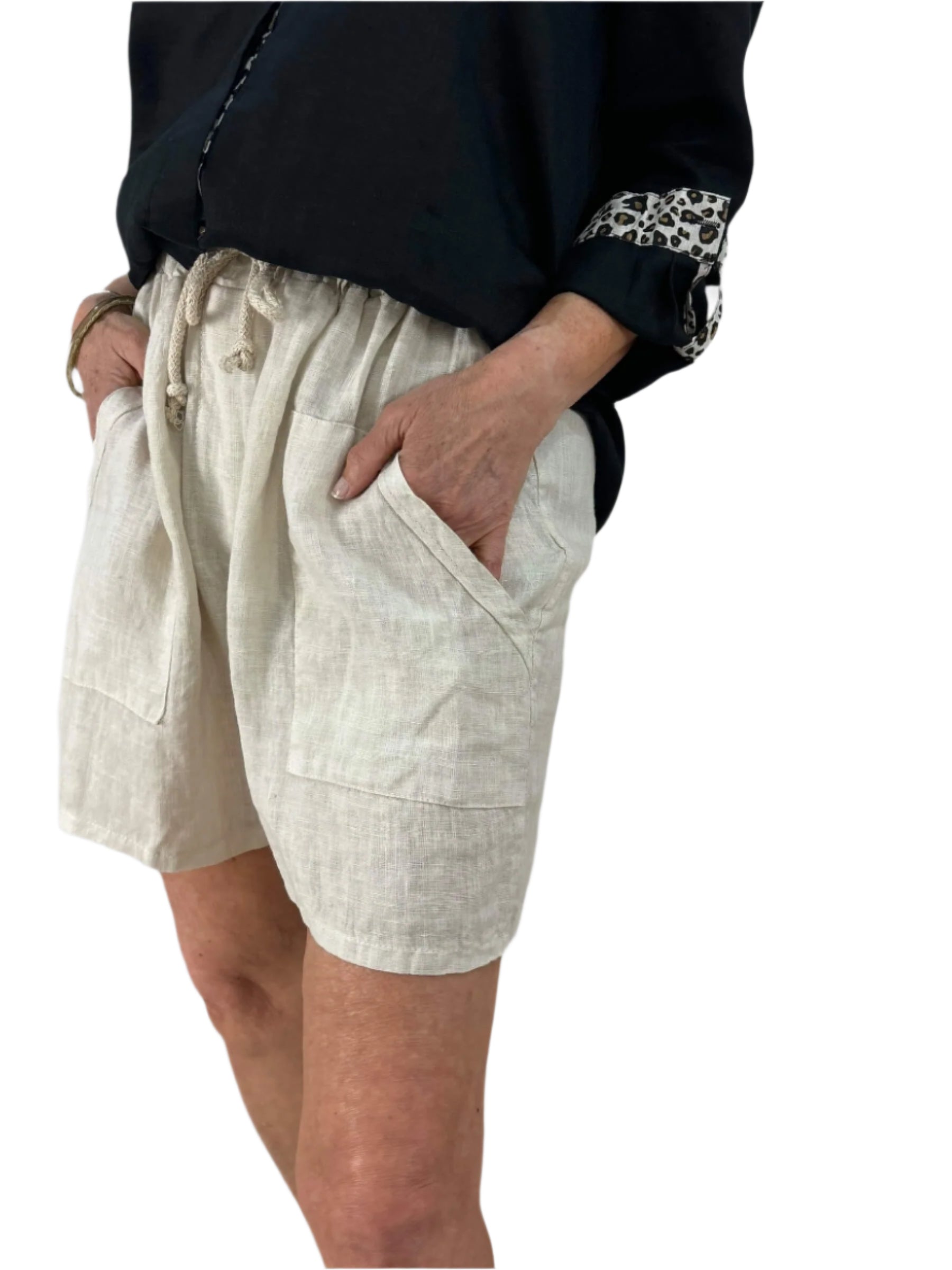 A woman dressed in a black shirt and natural shorts stands confidently, showcasing a casual summer outfit.