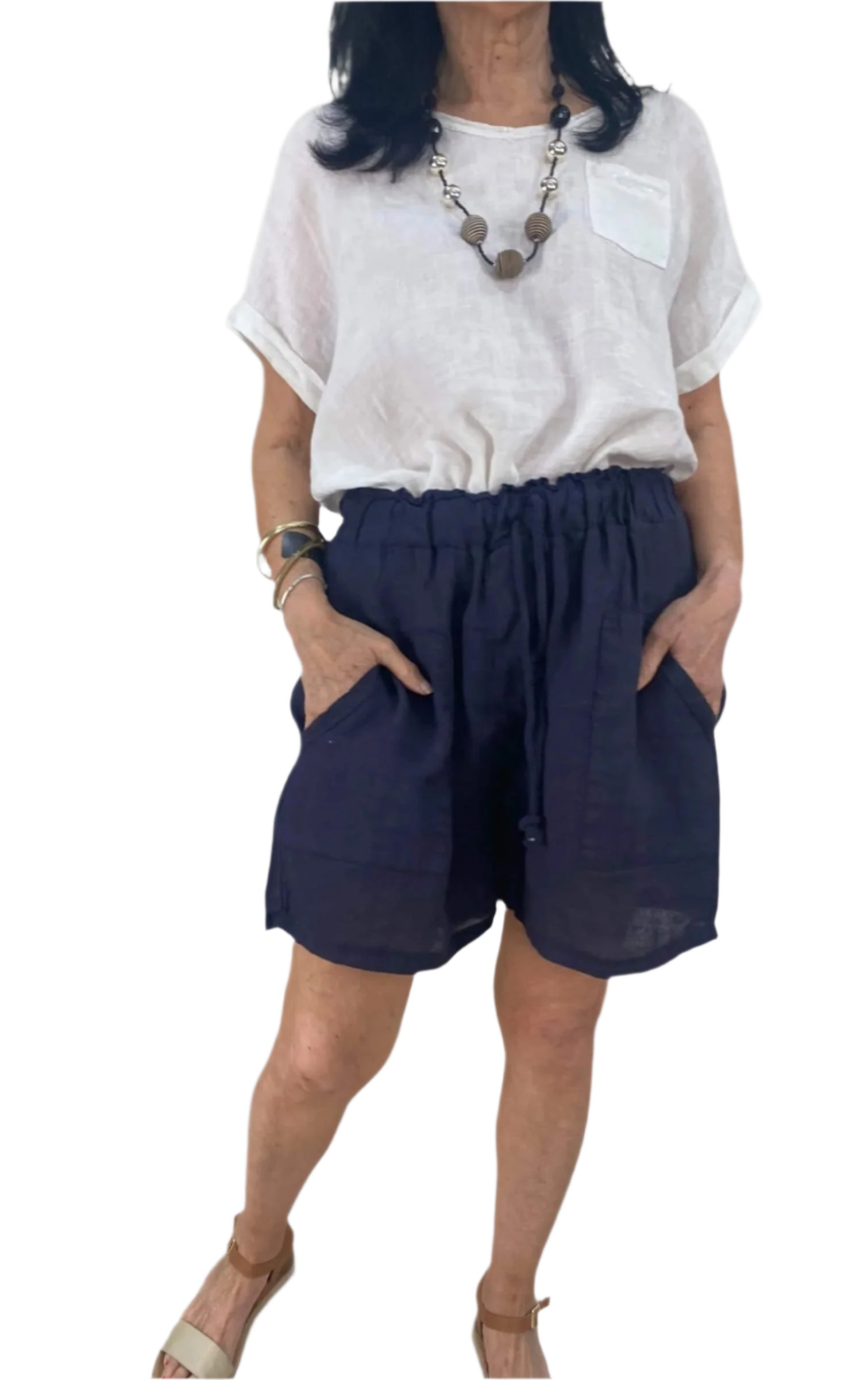 A woman dressed in a white shirt and blue shorts stands confidently, showcasing a casual summer outfit.