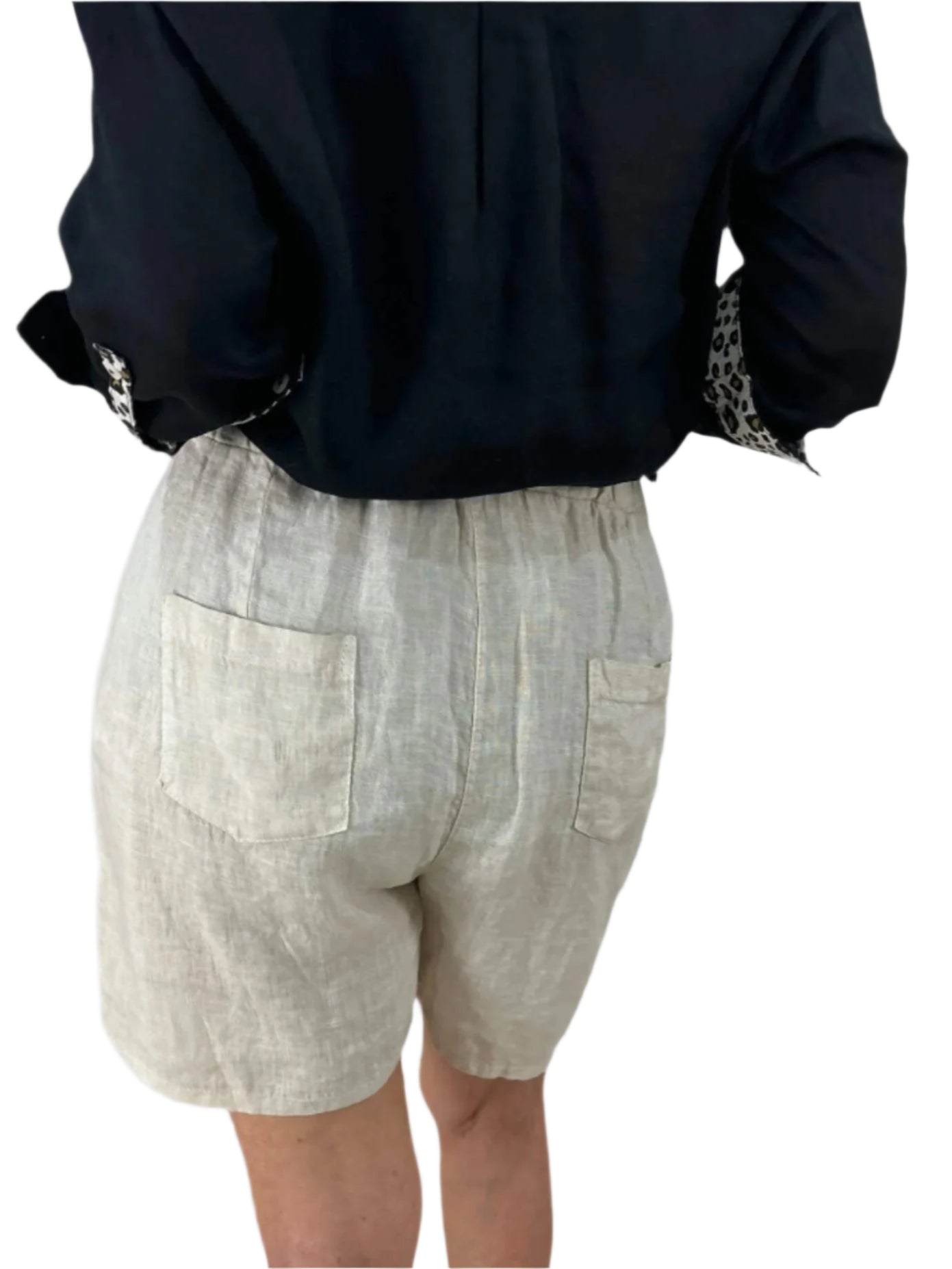 A woman dressed in a black shirt and natural shorts stands confidently, showcasing a casual summer outfit.