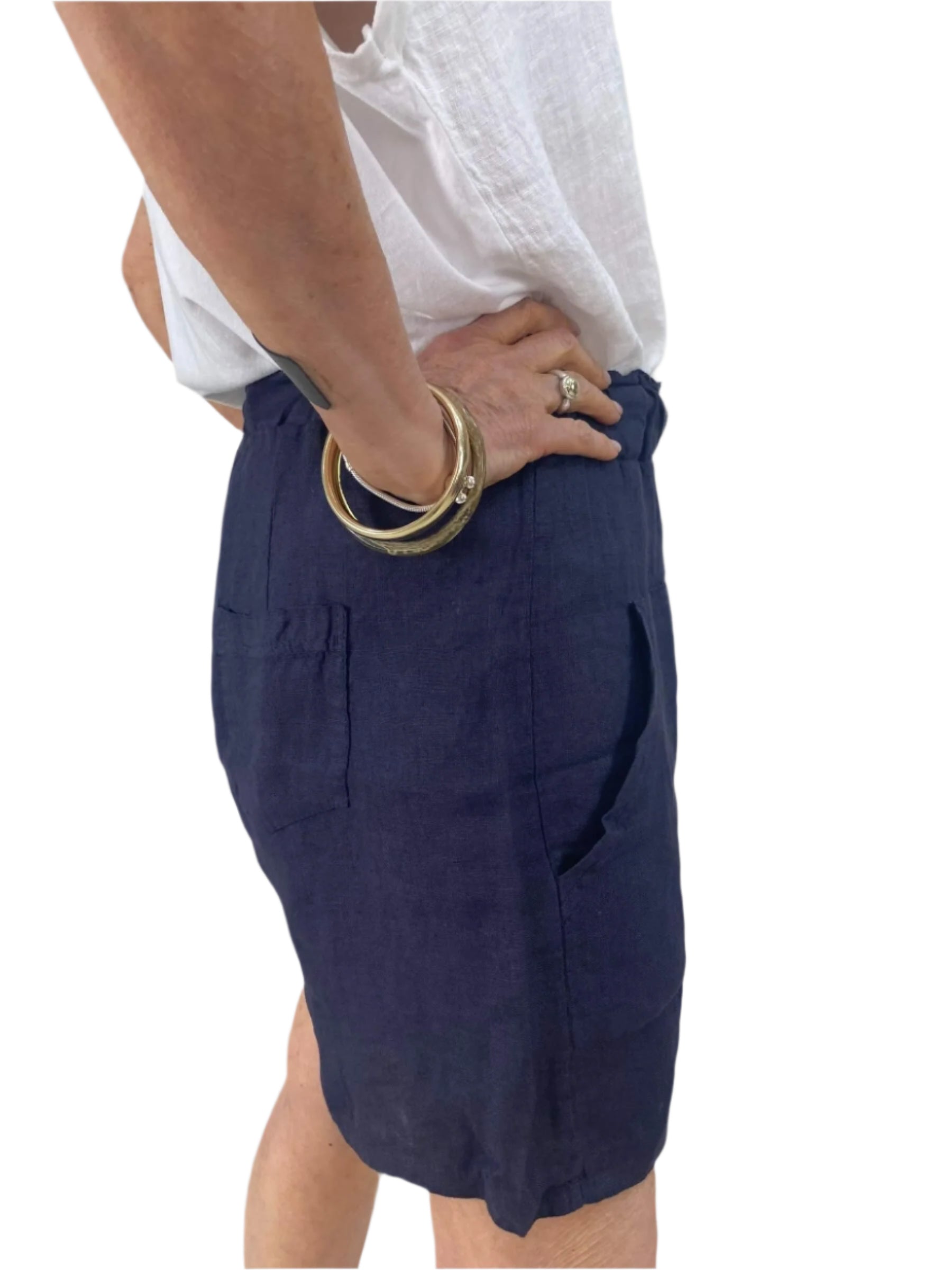 A woman dressed in a white shirt and blue shorts stands confidently, showcasing a casual summer outfit.