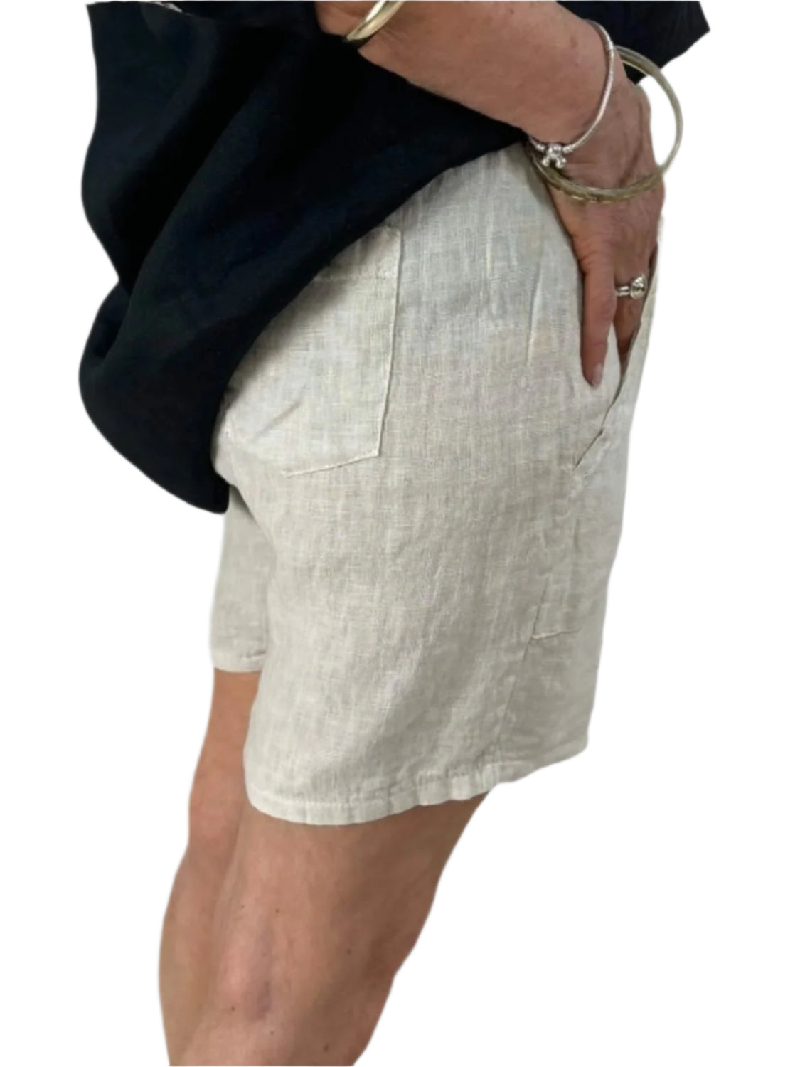 A woman dressed in a black shirt and natural shorts stands confidently, showcasing a casual summer outfit.