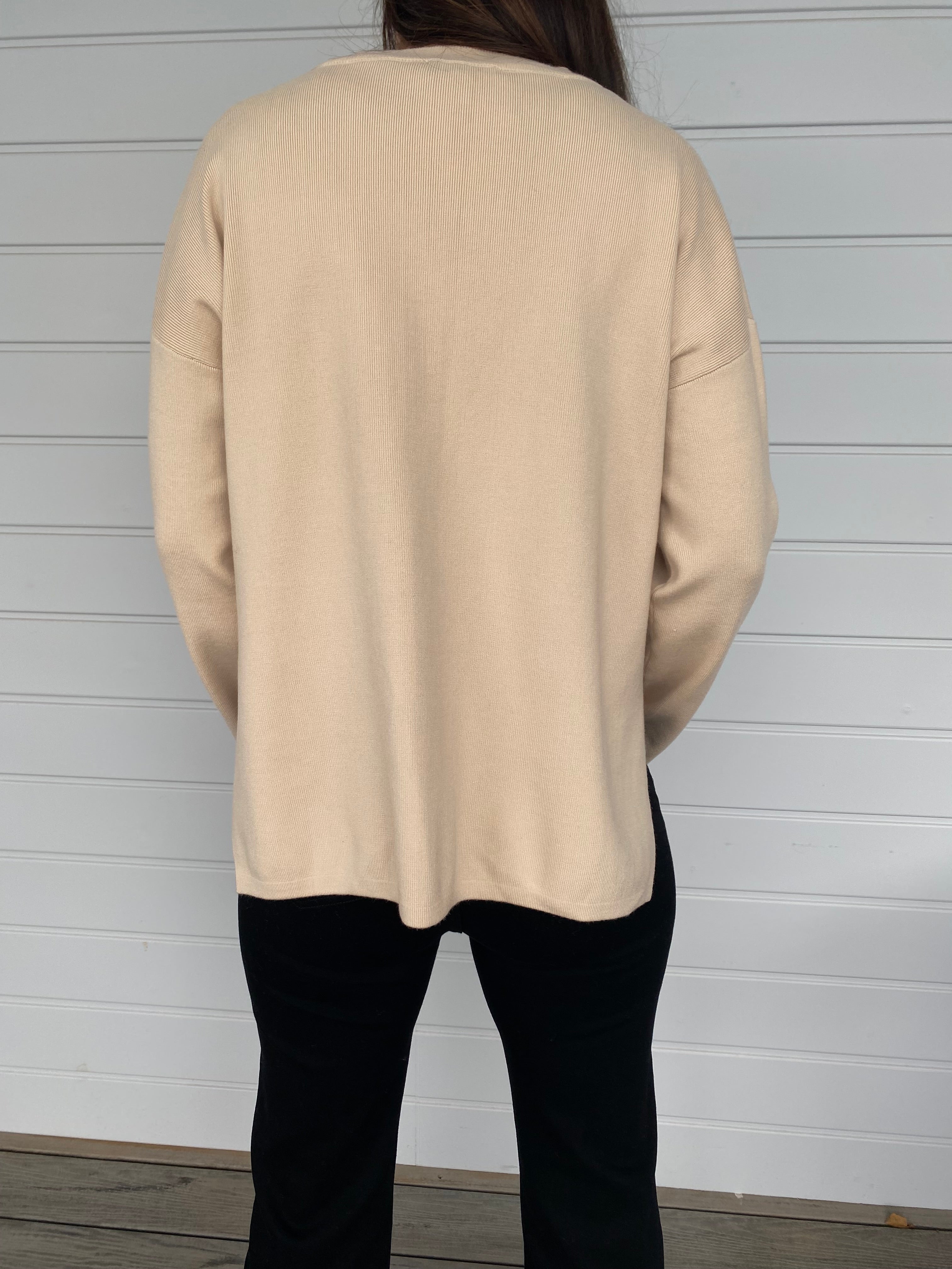 Women standing in a cream top and black denim jeans against a wall