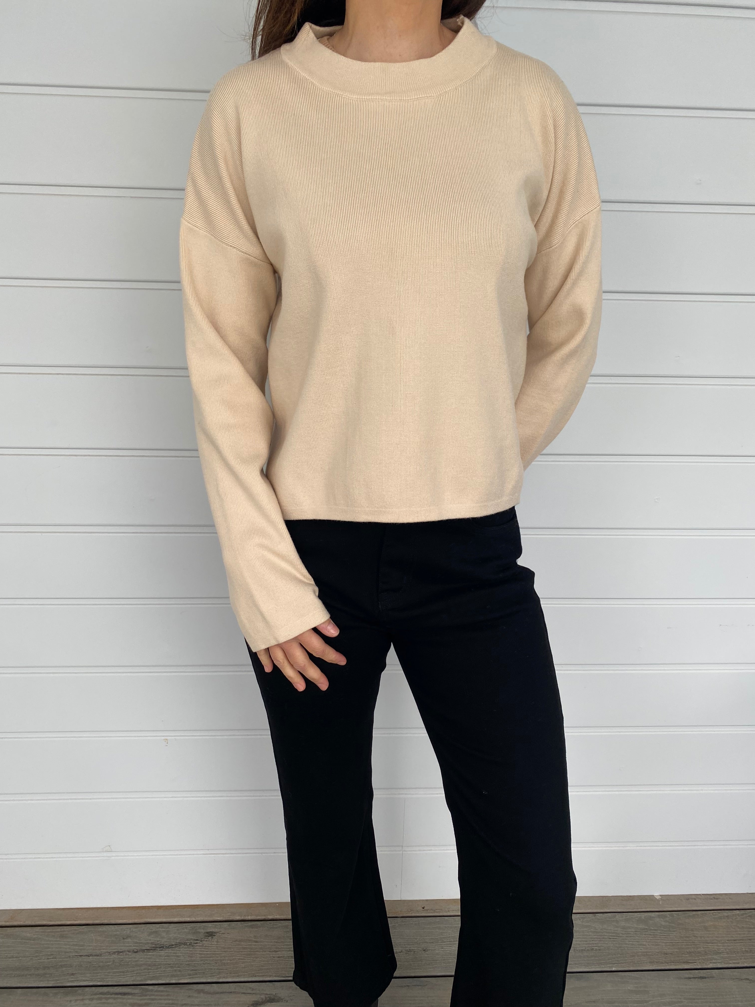 Women standing in a cream top and black denim jeans against a wall