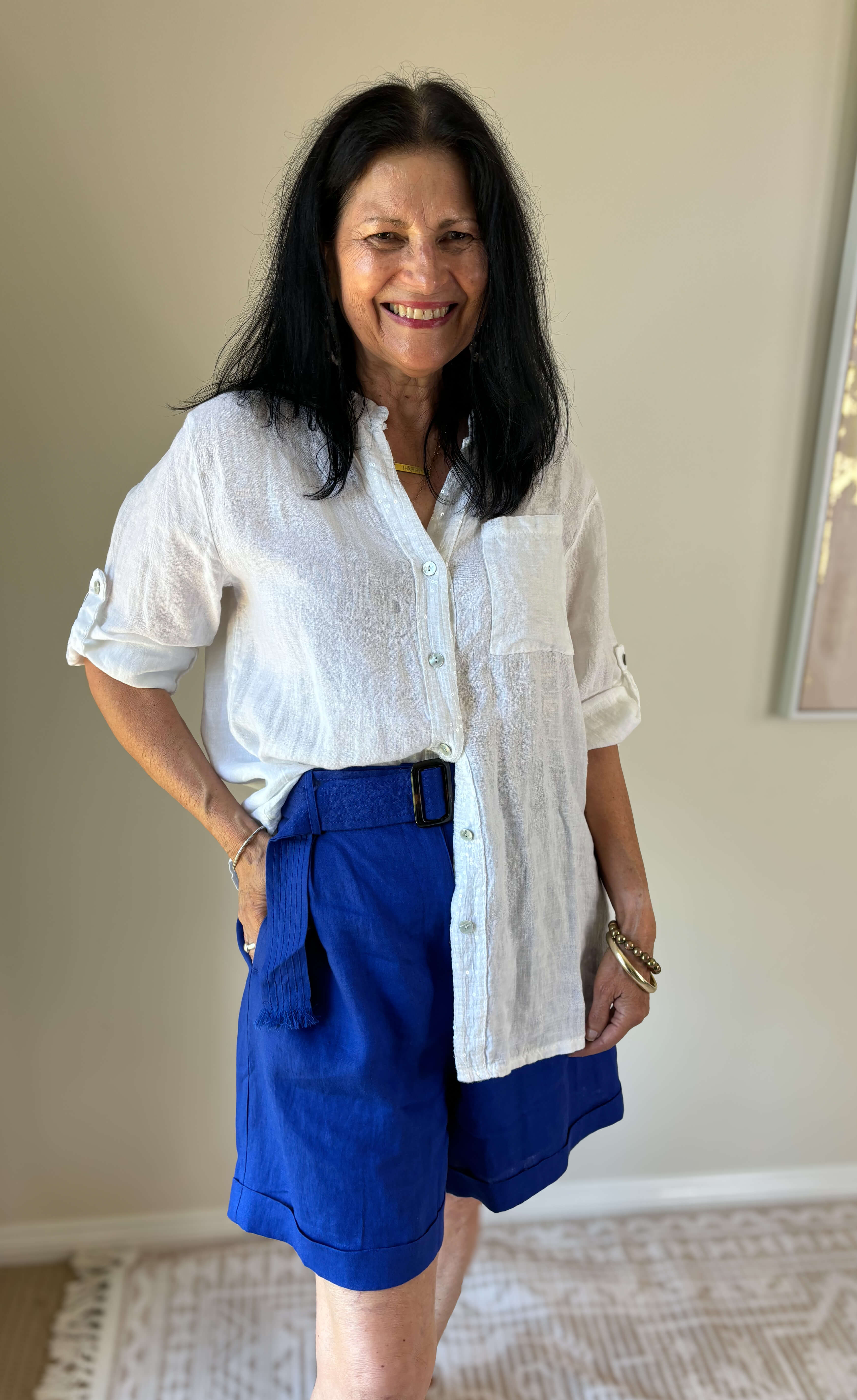 Lady smiling with hand in pocket in white shirt and blue shorts