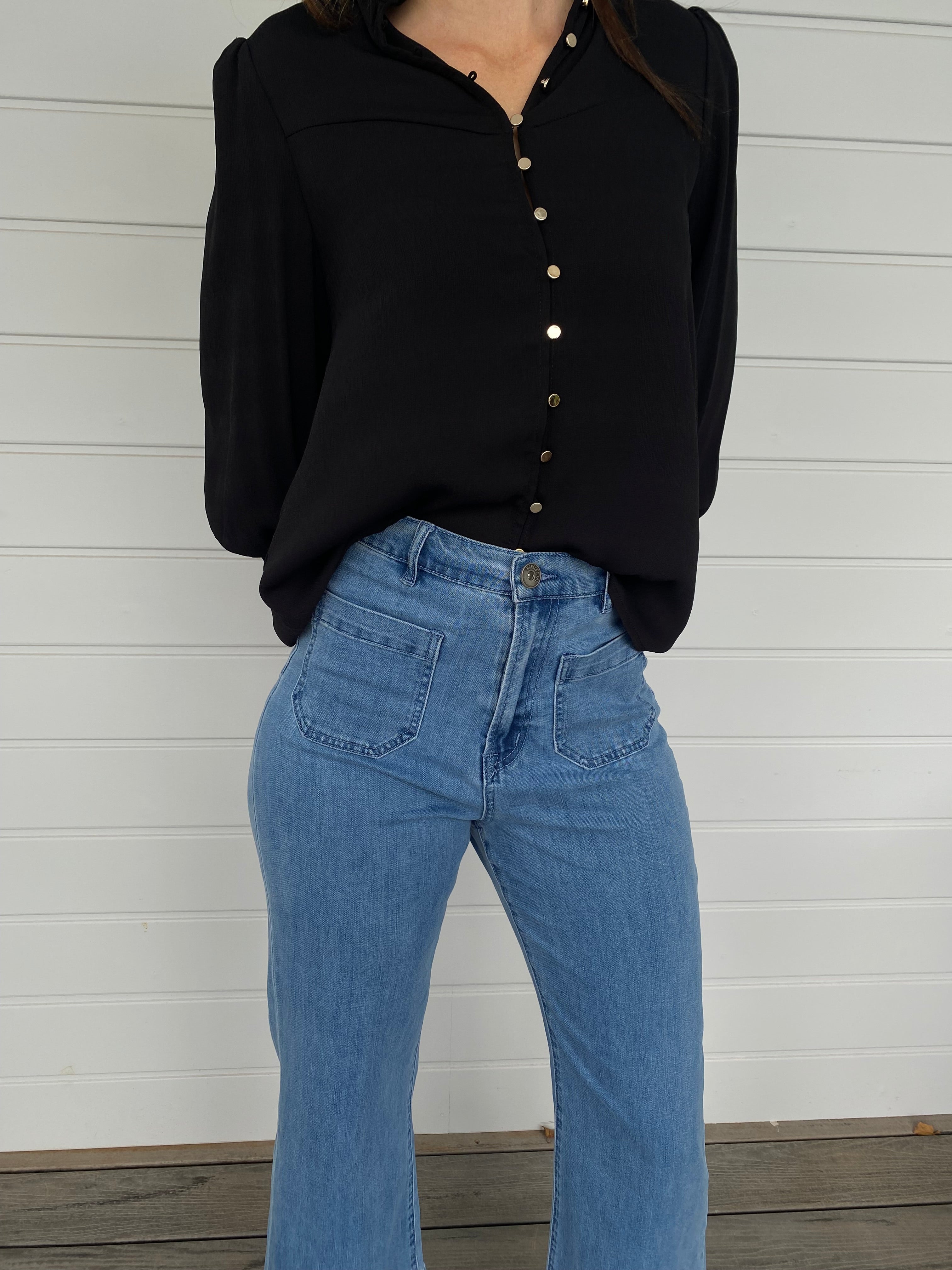 Woman standing in a black blouse with gold buttons and blue jeans