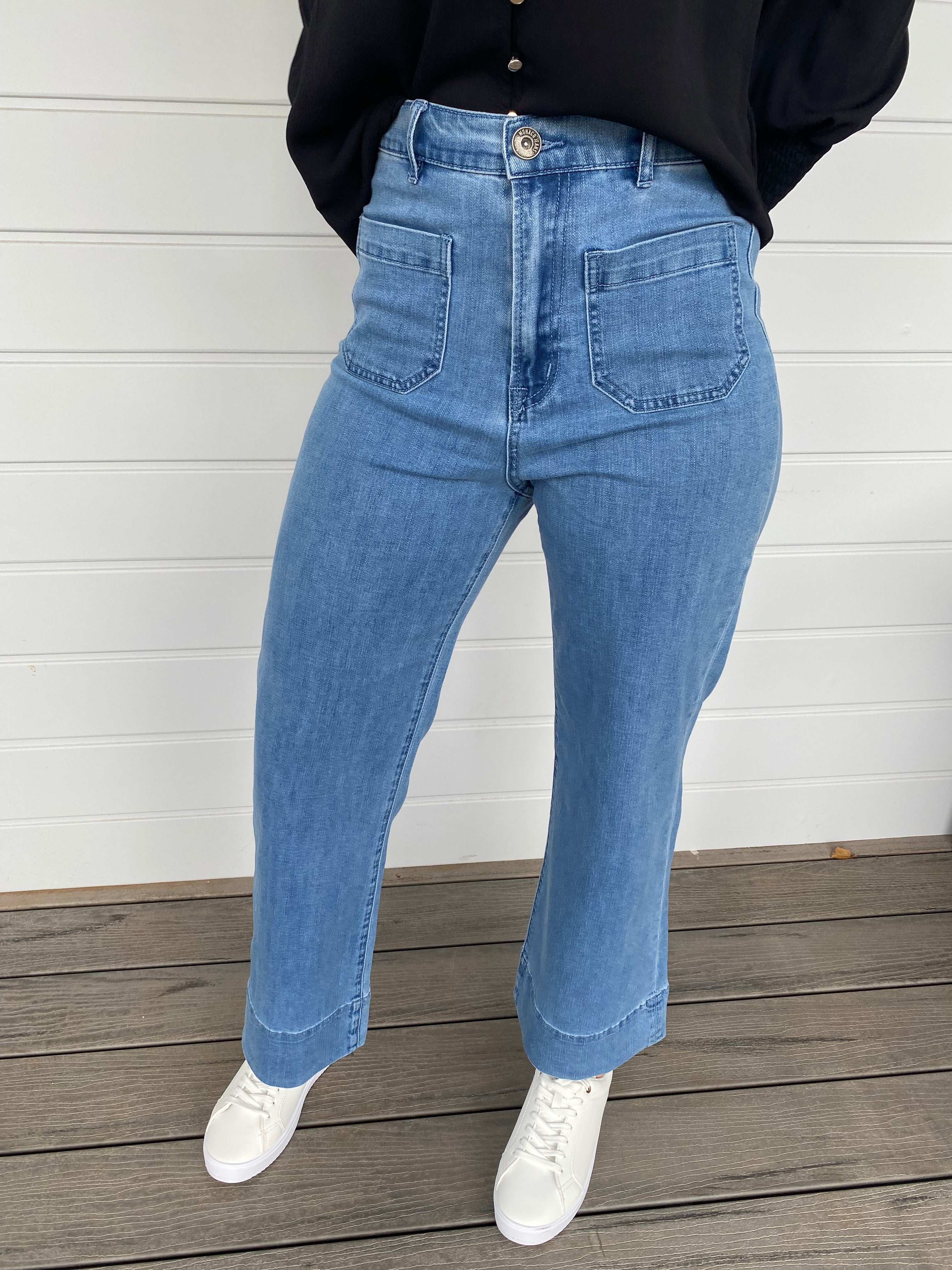 Women standing in blue denim jeans and black blouse with white sneakers