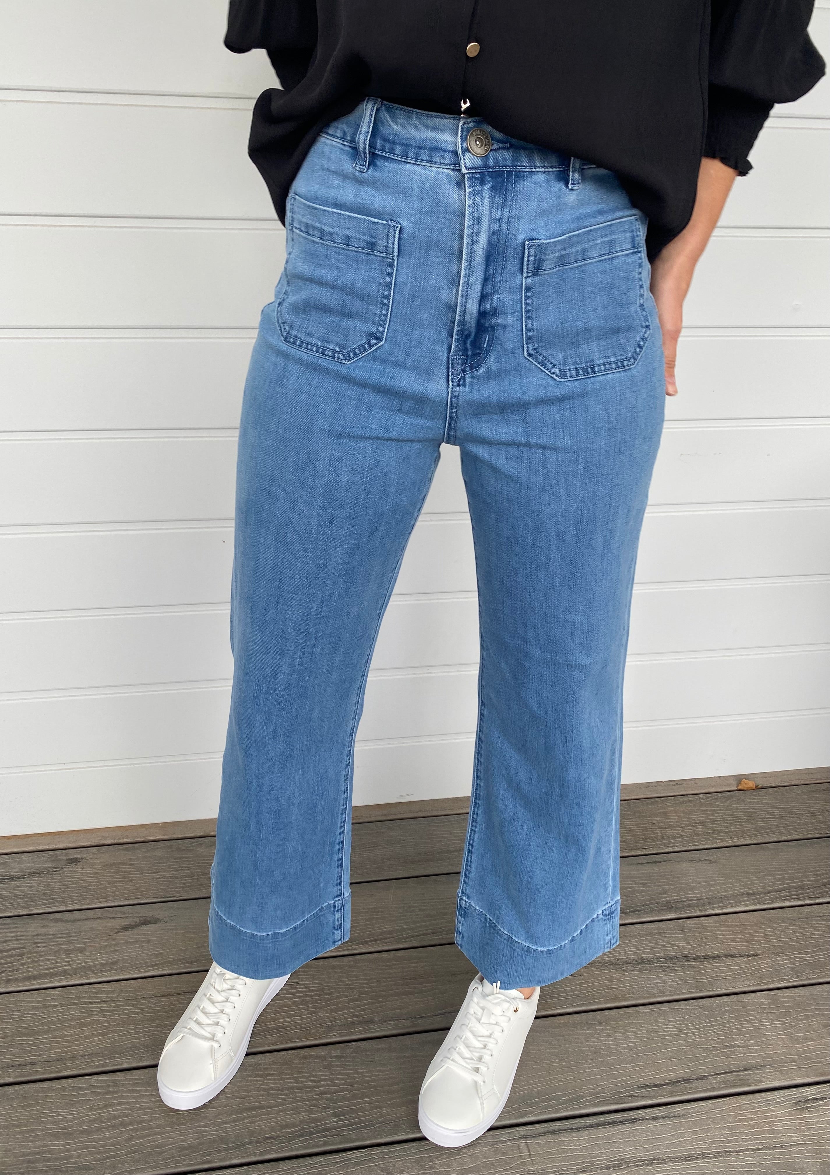 Women standing in blue denim jeans and black blouse with white sneakers
