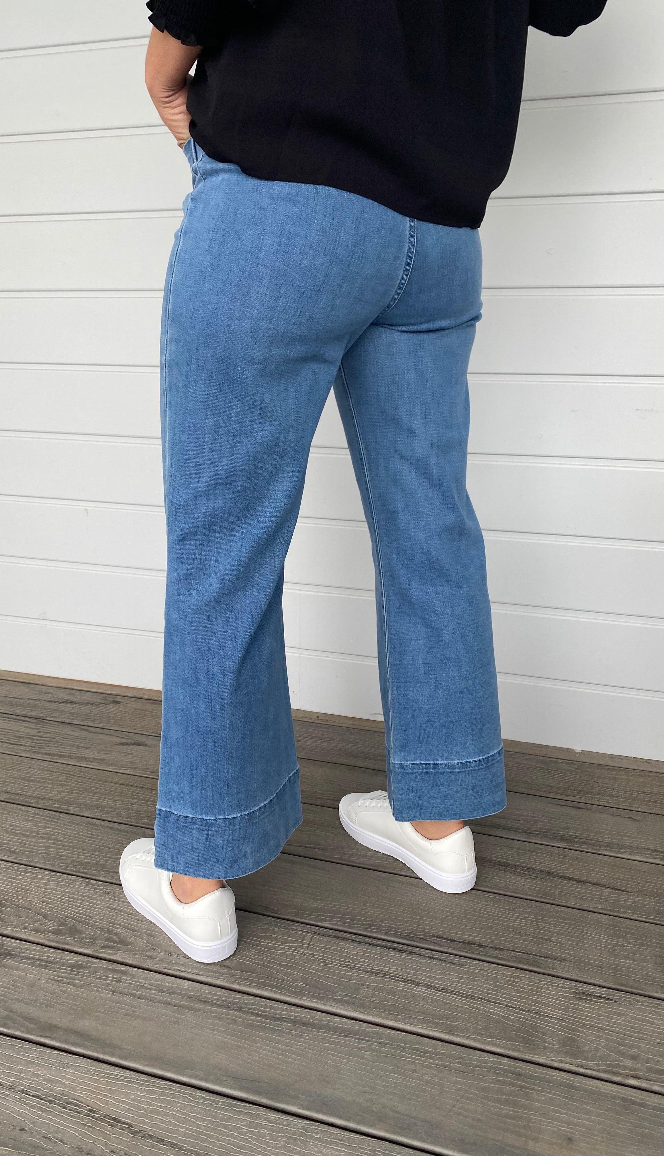 Women standing in blue denim jeans and black blouse with white sneakers