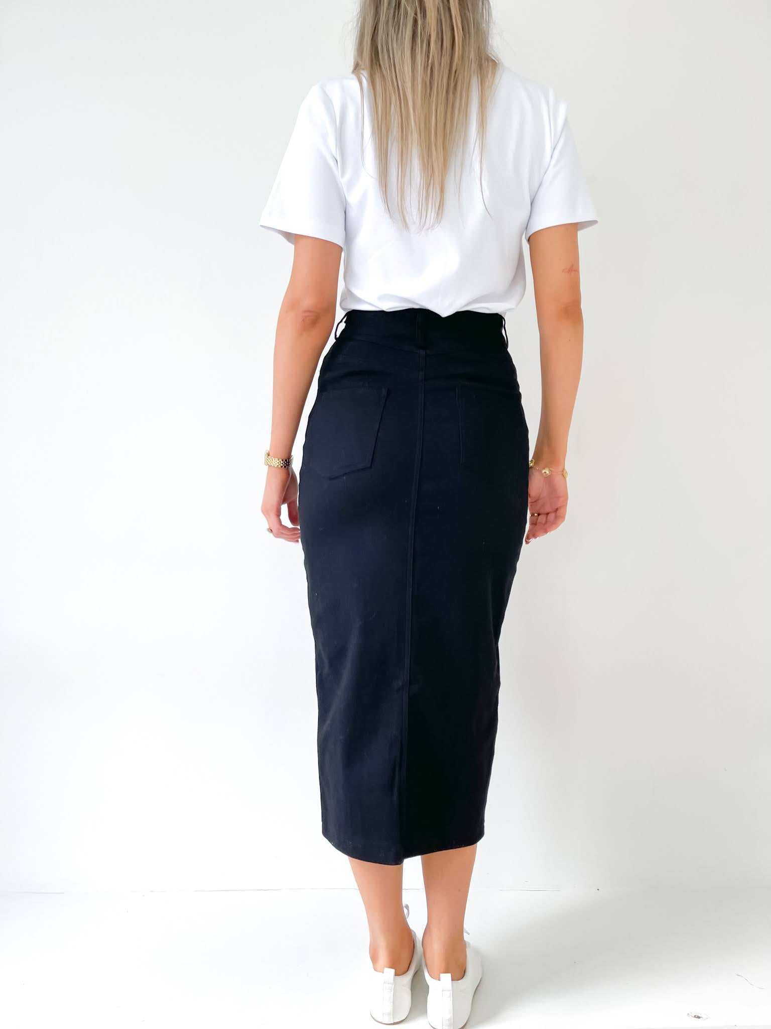 Woman standing in a black denim skirt and white top with a white background and white sneakers