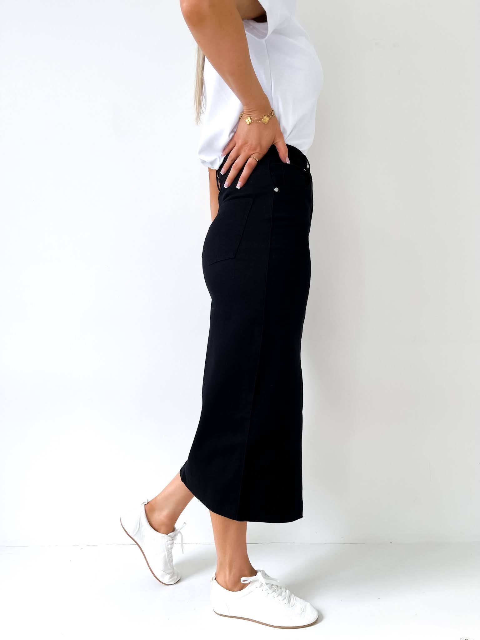 Woman standing in a black denim skirt and white top with a white background
