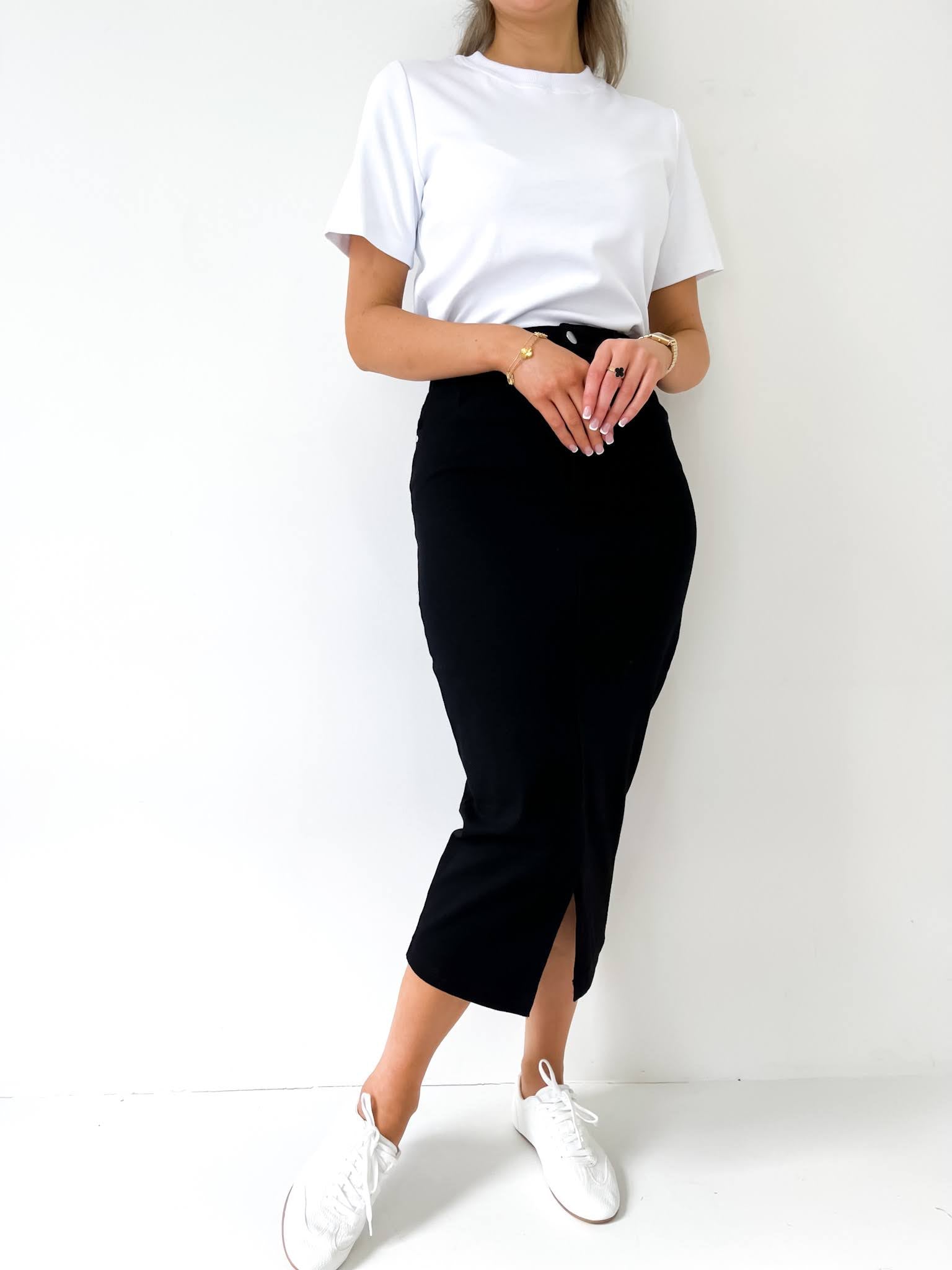 Woman standing in a black denim skirt and white top with a white background