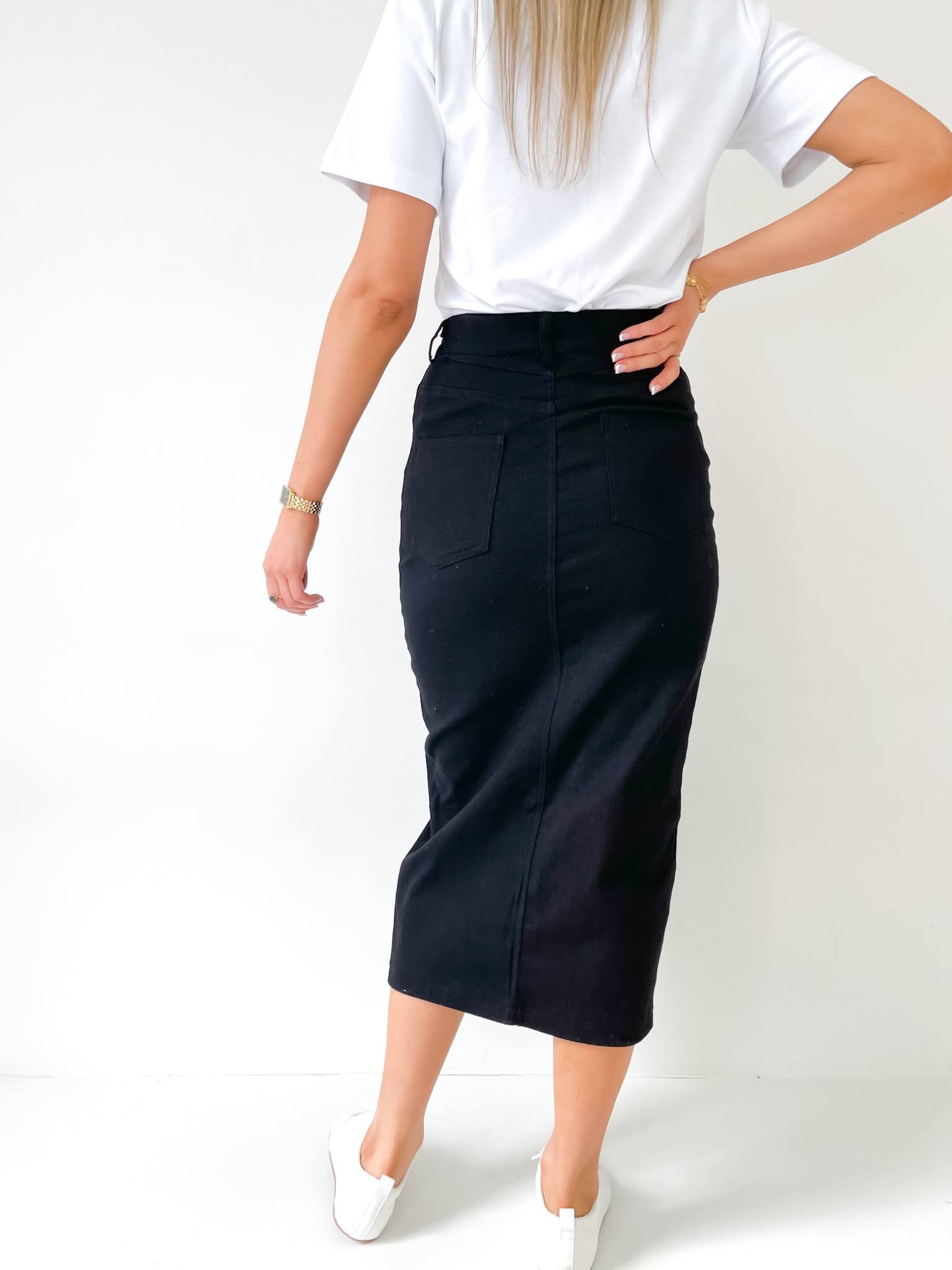 Woman standing in a black denim skirt and white top with a white background and white sneakers