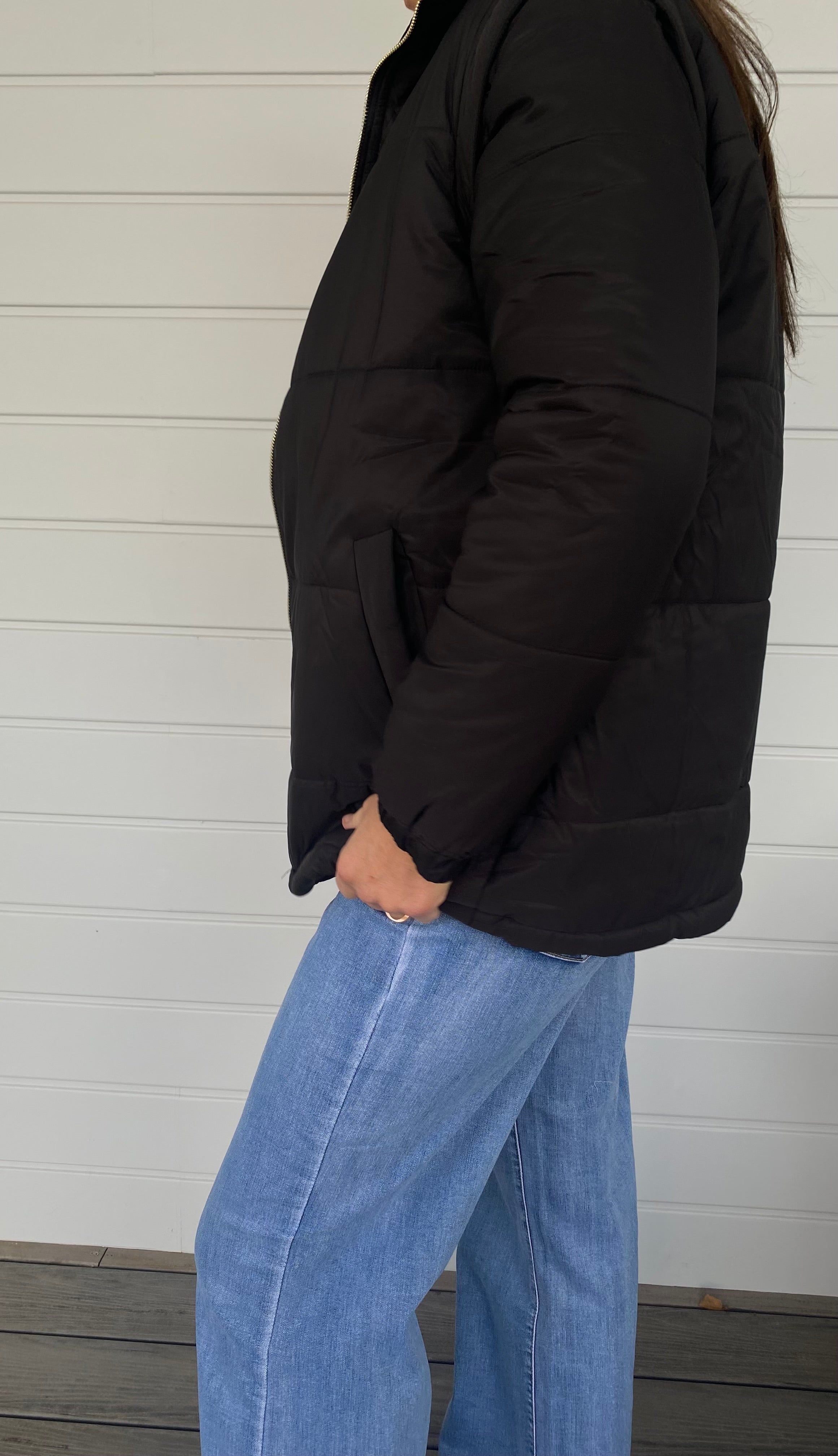 Woman standing in a black puffer jacket with blue jeans