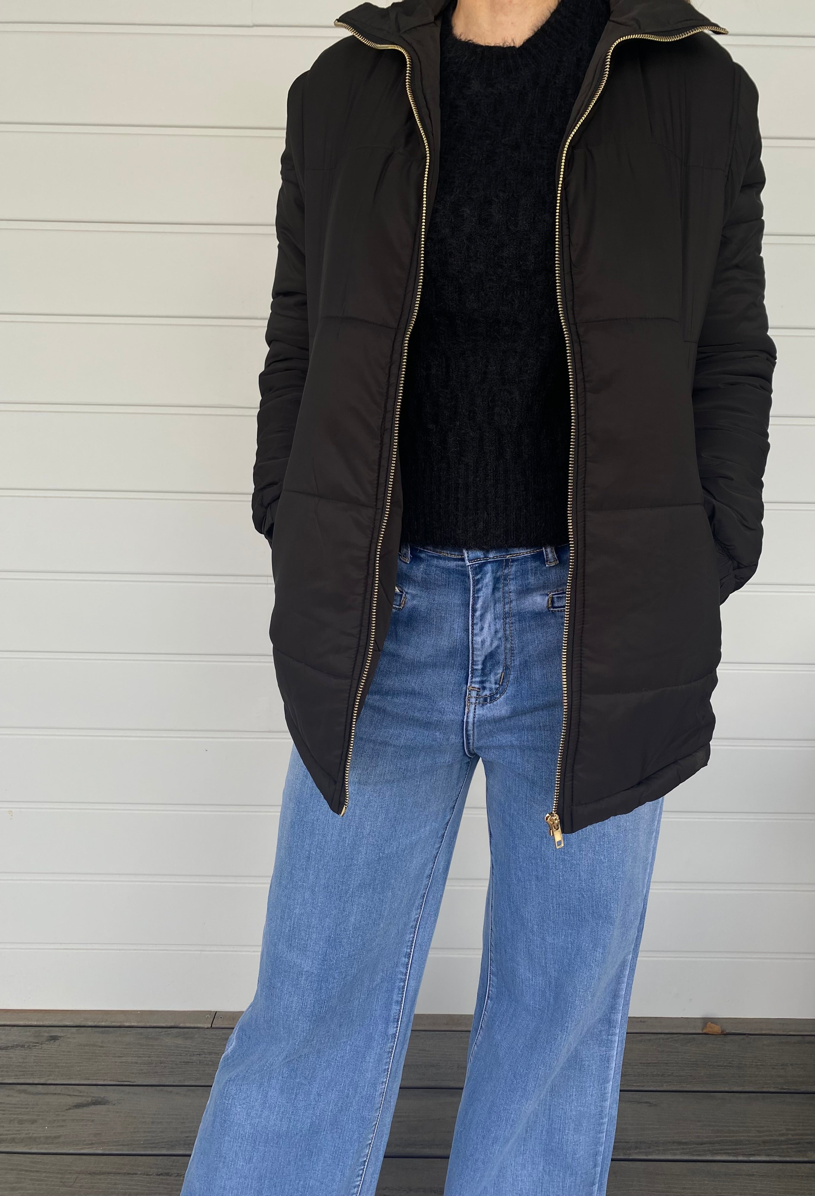Woman standing in a black puffer jacket with blue jeans