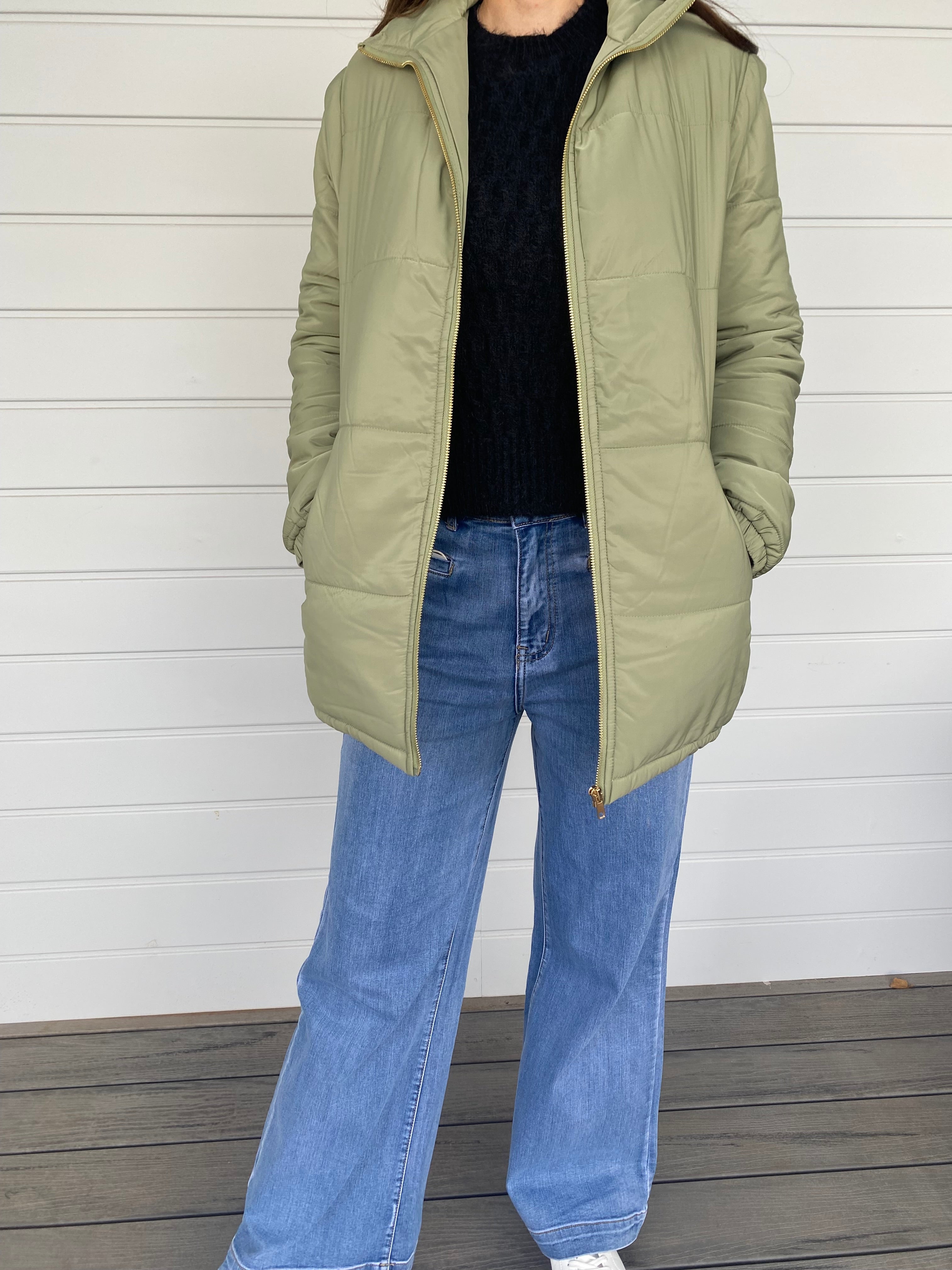 Woman standing in a green puffer jacket with blue jeans