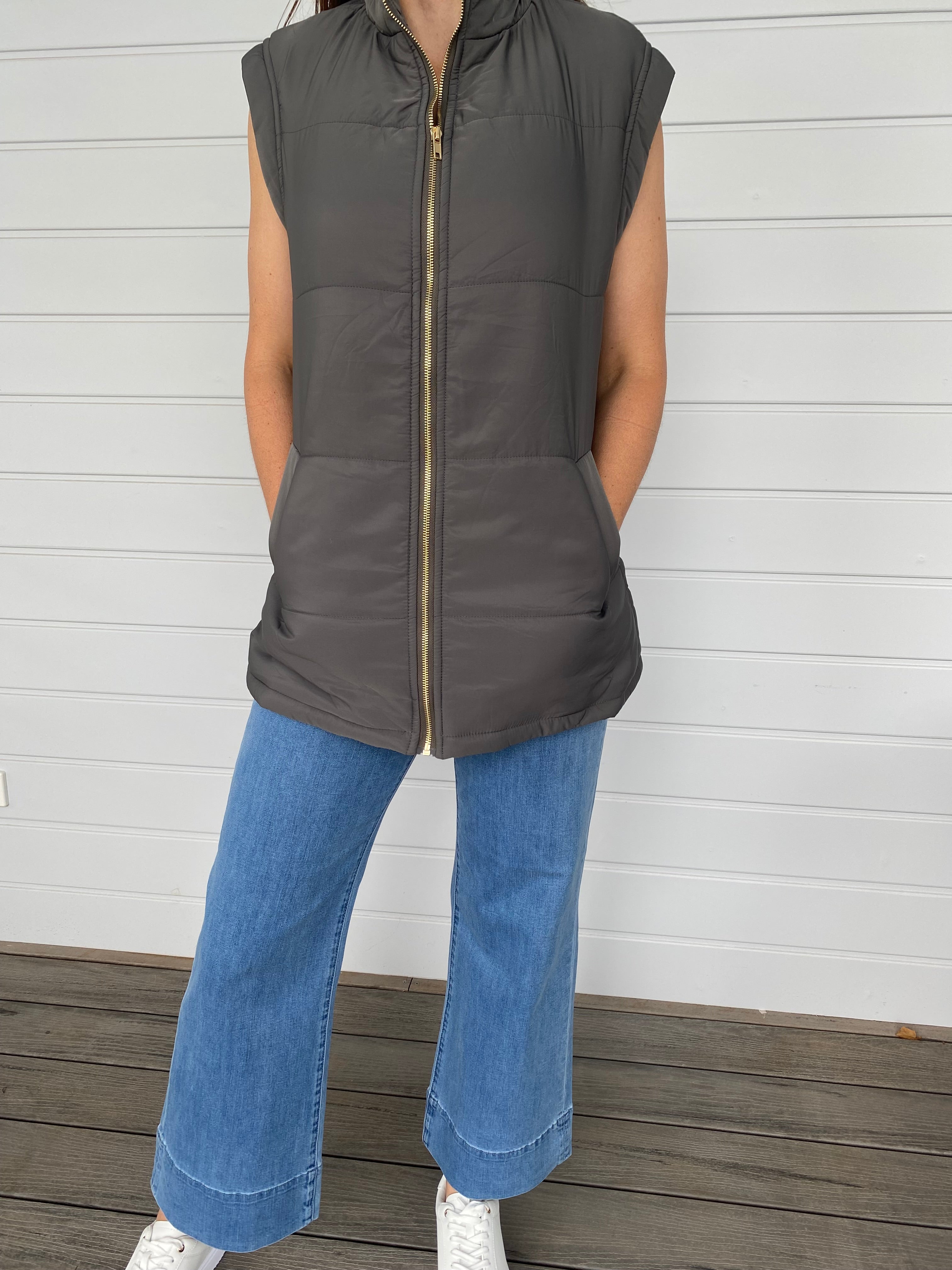 Woman standing in a grey puffer jacket with blue jeans