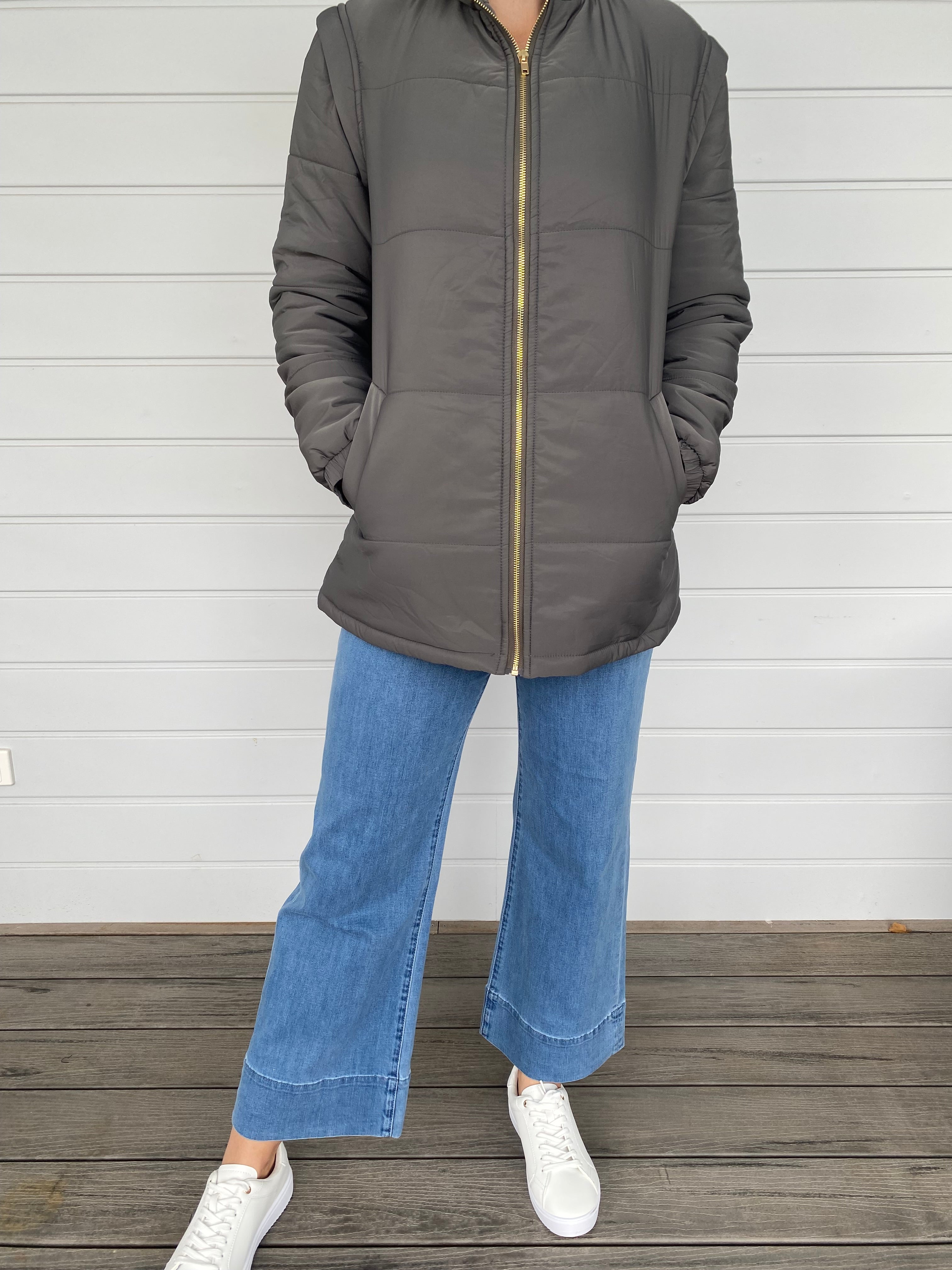 Woman standing in a grey puffer jacket with blue jeans