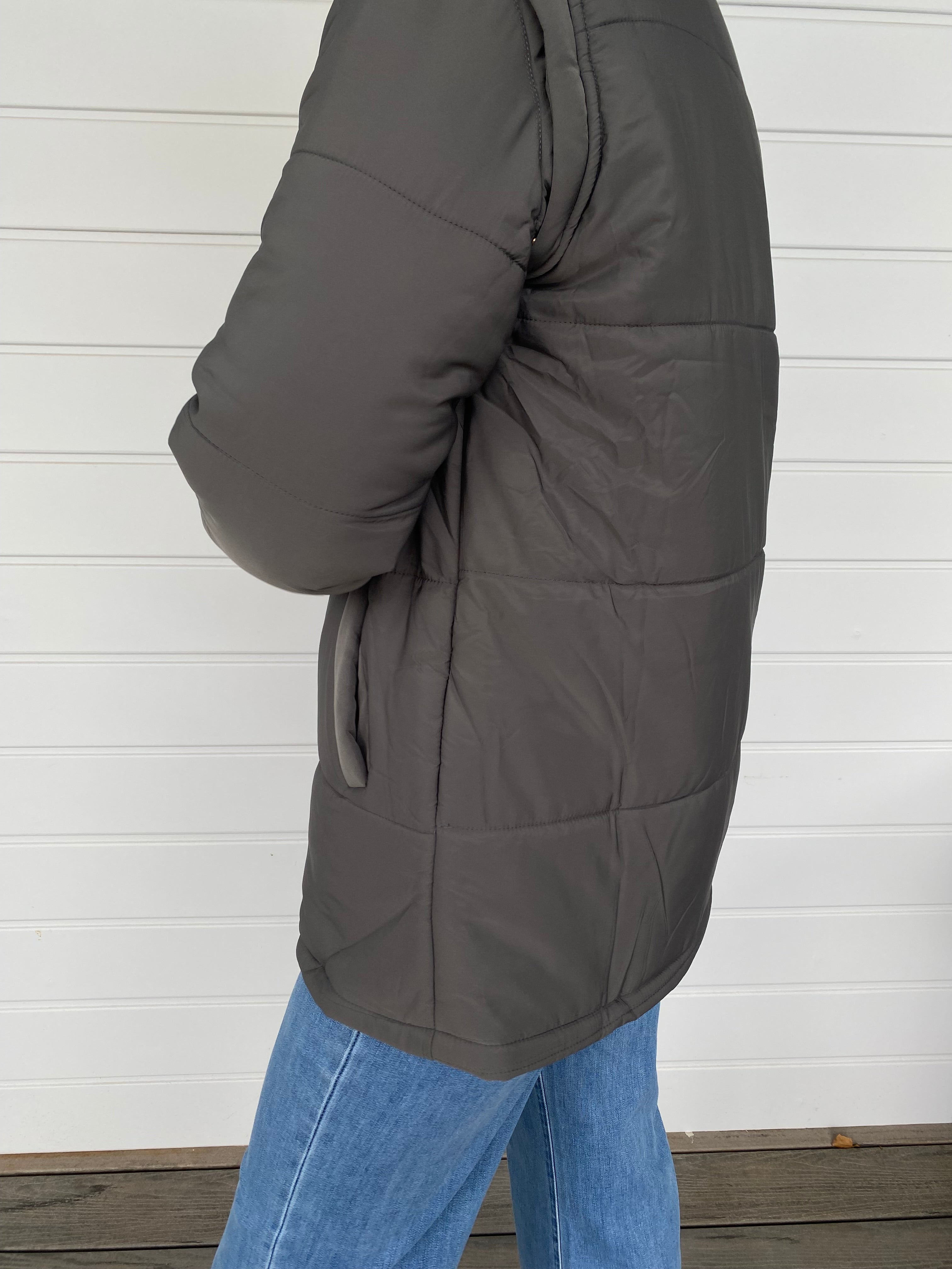 Woman standing in a grey puffer jacket with blue jeans