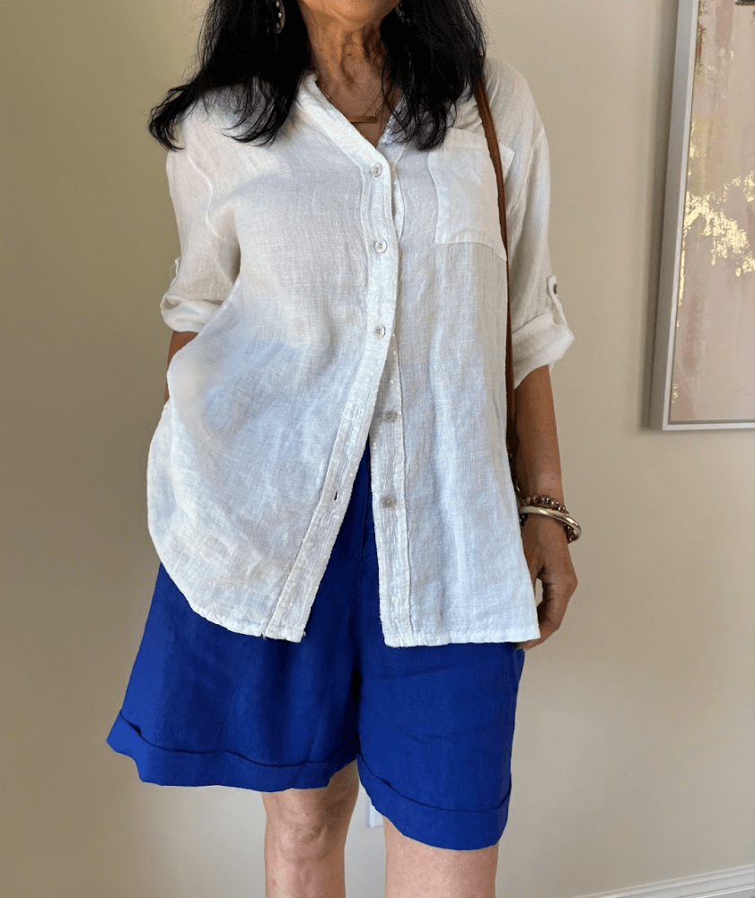 Lady standing in a white shirt and blue shorts against a wall