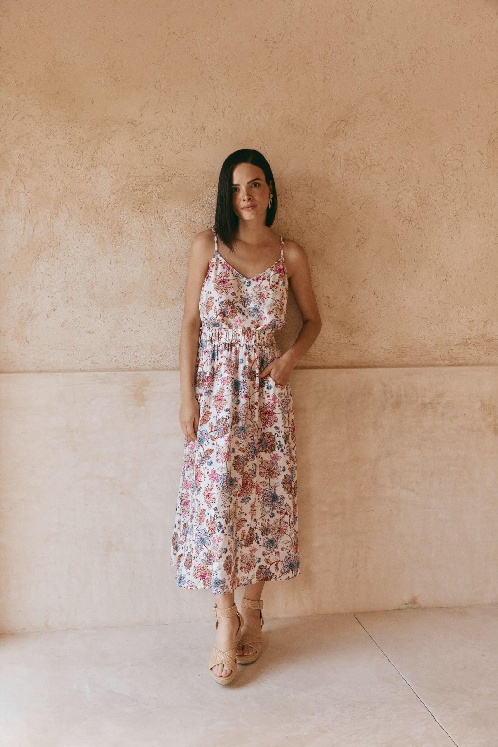 A woman in a floral skirt leans casually against a wall, exuding a relaxed and stylish vibe.
