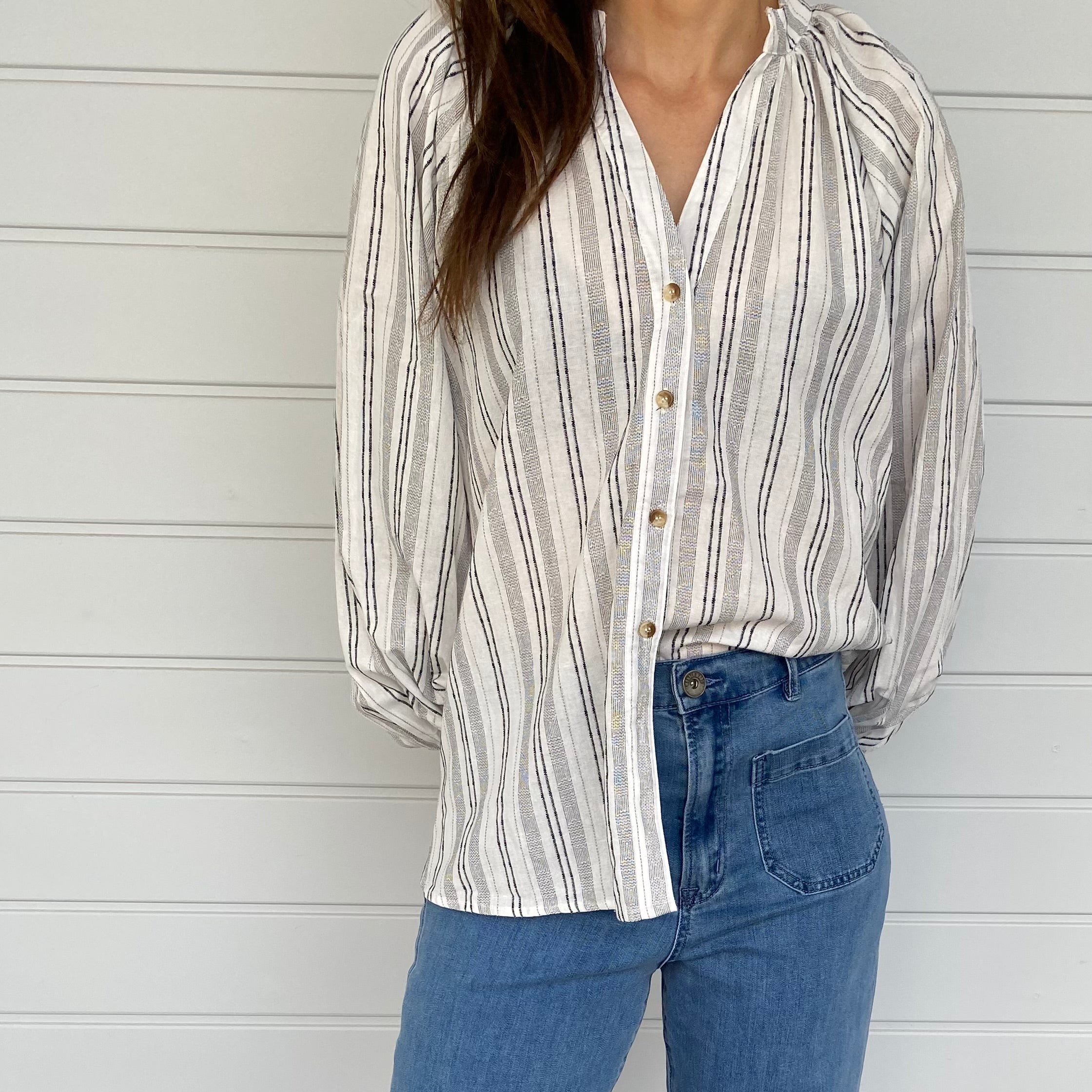 A woman in jeans and a striped shirt stands confidently, showcasing a casual and stylish outfit.