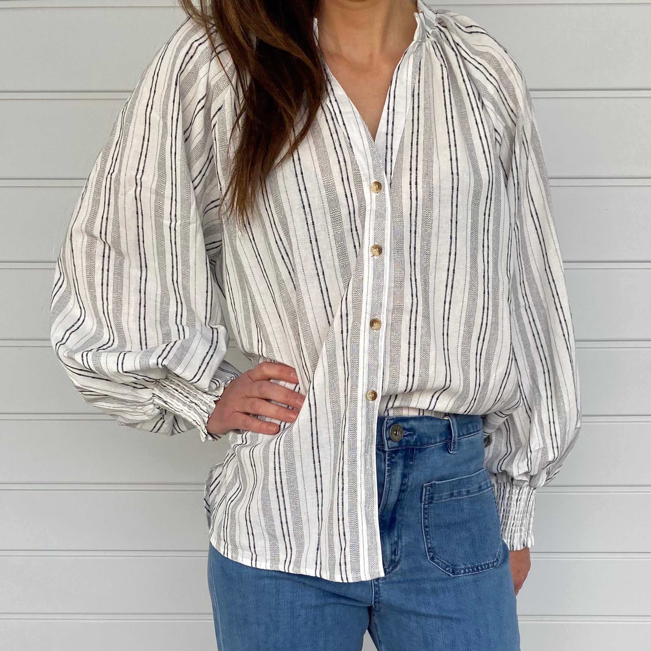 A woman in jeans and a striped shirt stands confidently, showcasing a casual and stylish outfit.
