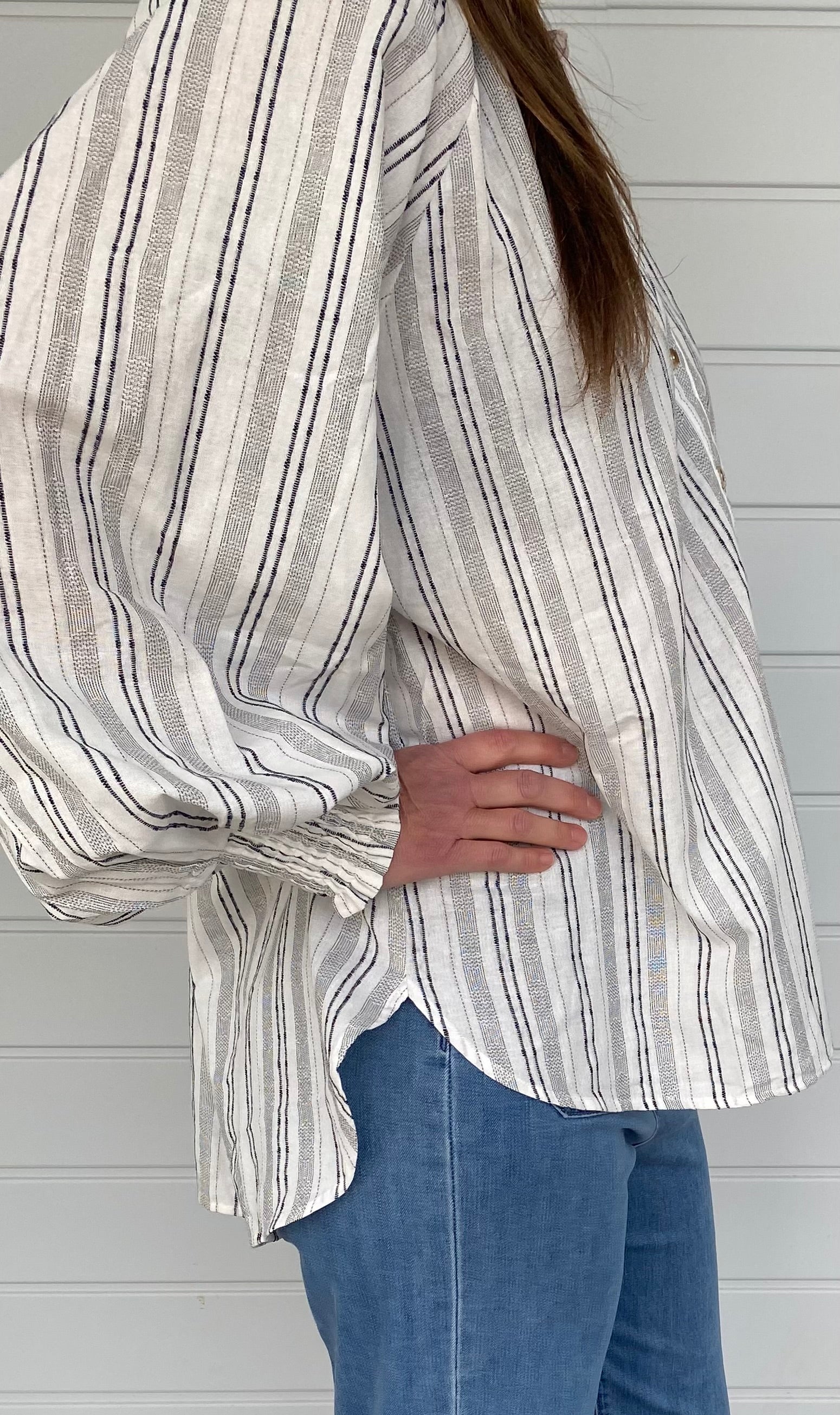A woman in jeans and a striped shirt stands confidently, showcasing a casual and stylish outfit.