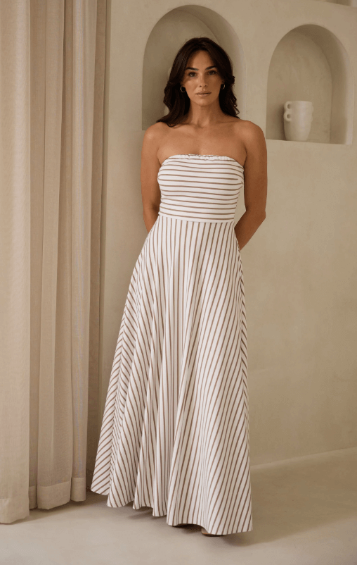 Model in brown and white strapless dress against a cream wall