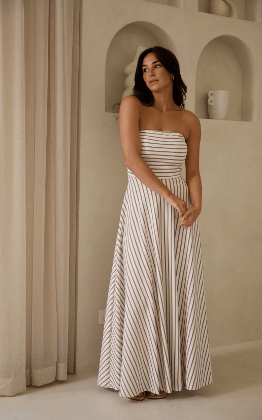 Model in brown and white strapless dress against a cream wall
