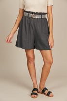  A model displays a fashionable outfit featuring a cream ribbed top and charcol grey shorts with black and white belt