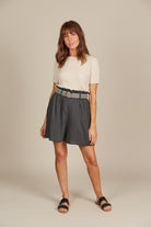 Woman in a fashionable outfit featuring a cream ribbed top and charcol grey shorts with black and white belt