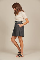 Woman in a fashionable outfit featuring a cream ribbed top and charcol grey shorts with black and white belt