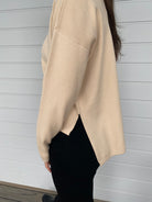 Women standing in a cream top and black denim jeans against a wall