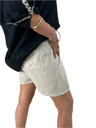 A woman dressed in a black shirt and natural shorts stands confidently, showcasing a casual summer outfit.