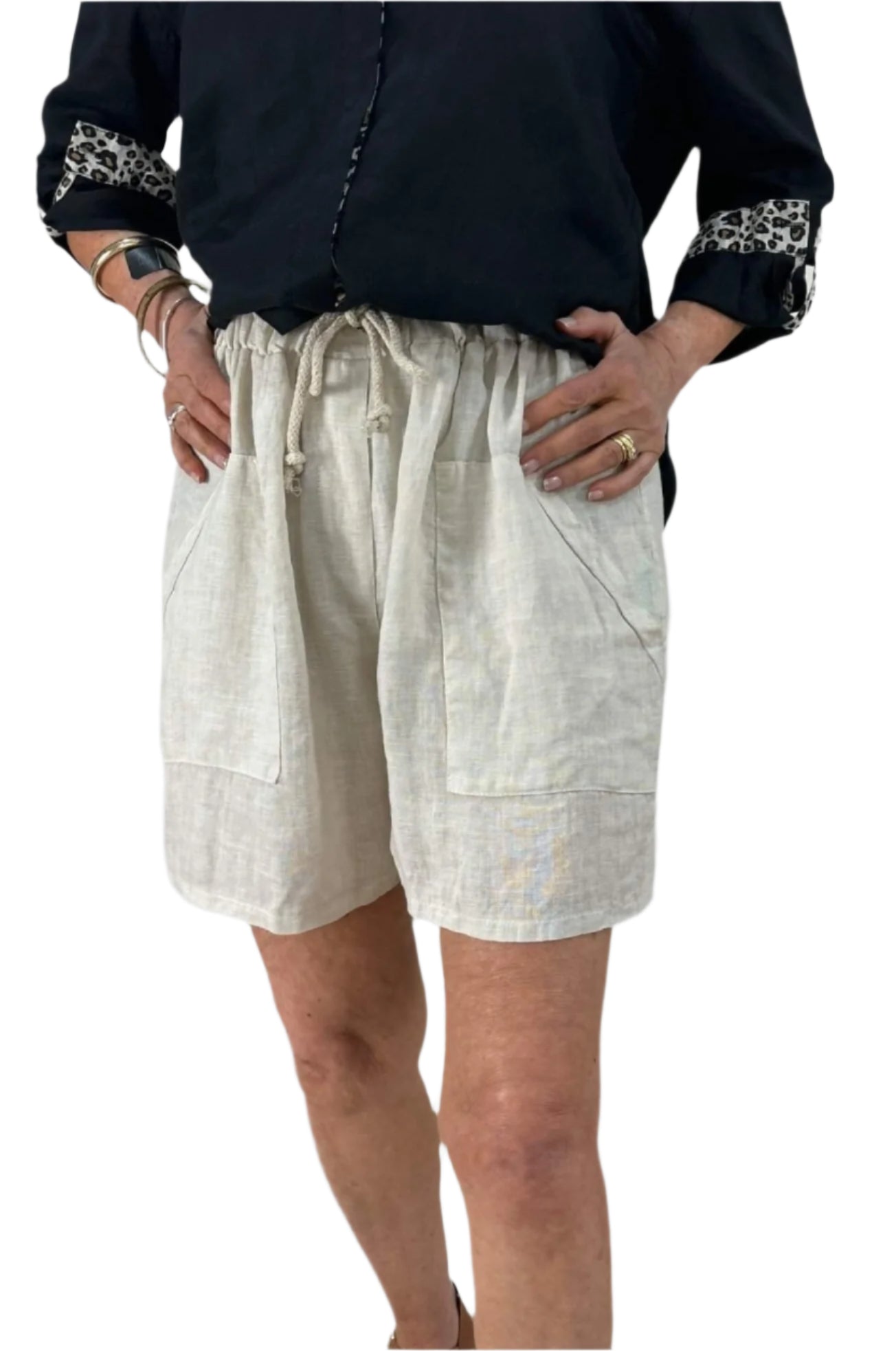 A woman dressed in a black shirt and natural shorts stands confidently, showcasing a casual summer outfit.