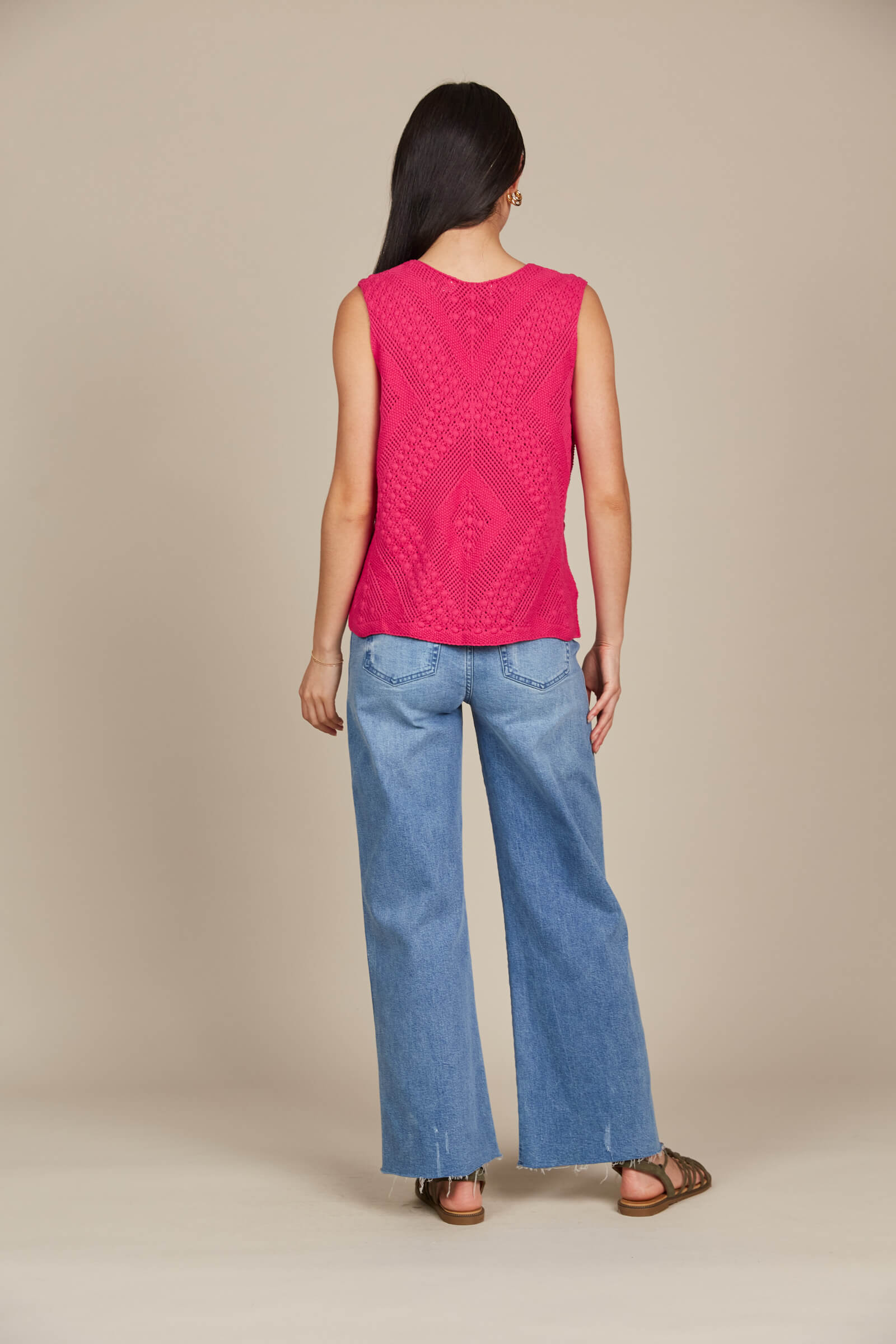 A woman seen from the back, wearing a pink top and jeans, standing confidently in a casual setting.