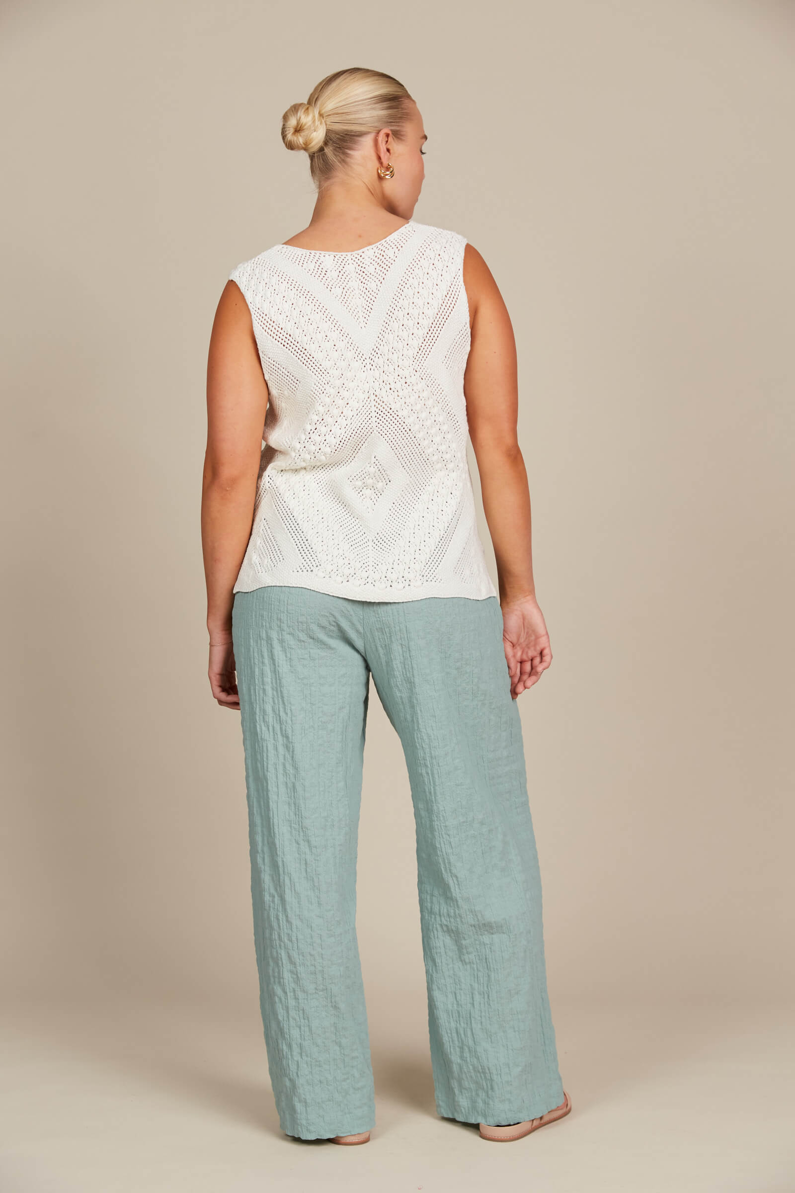 Back of A woman wearing a white top and blue pants, standing confidently in a casual setting.