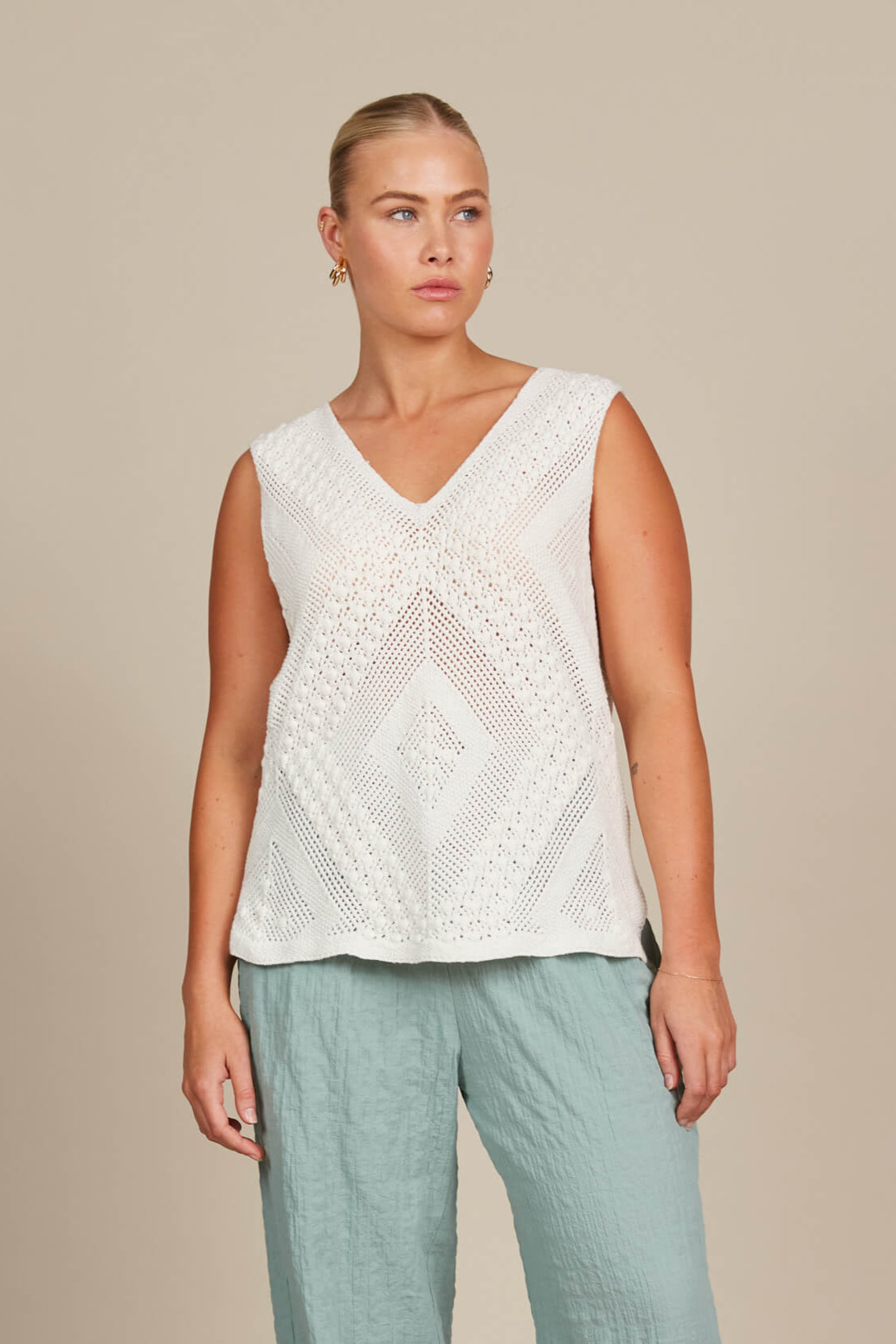 A woman wearing a white top and blue pants, standing confidently in a casual setting.